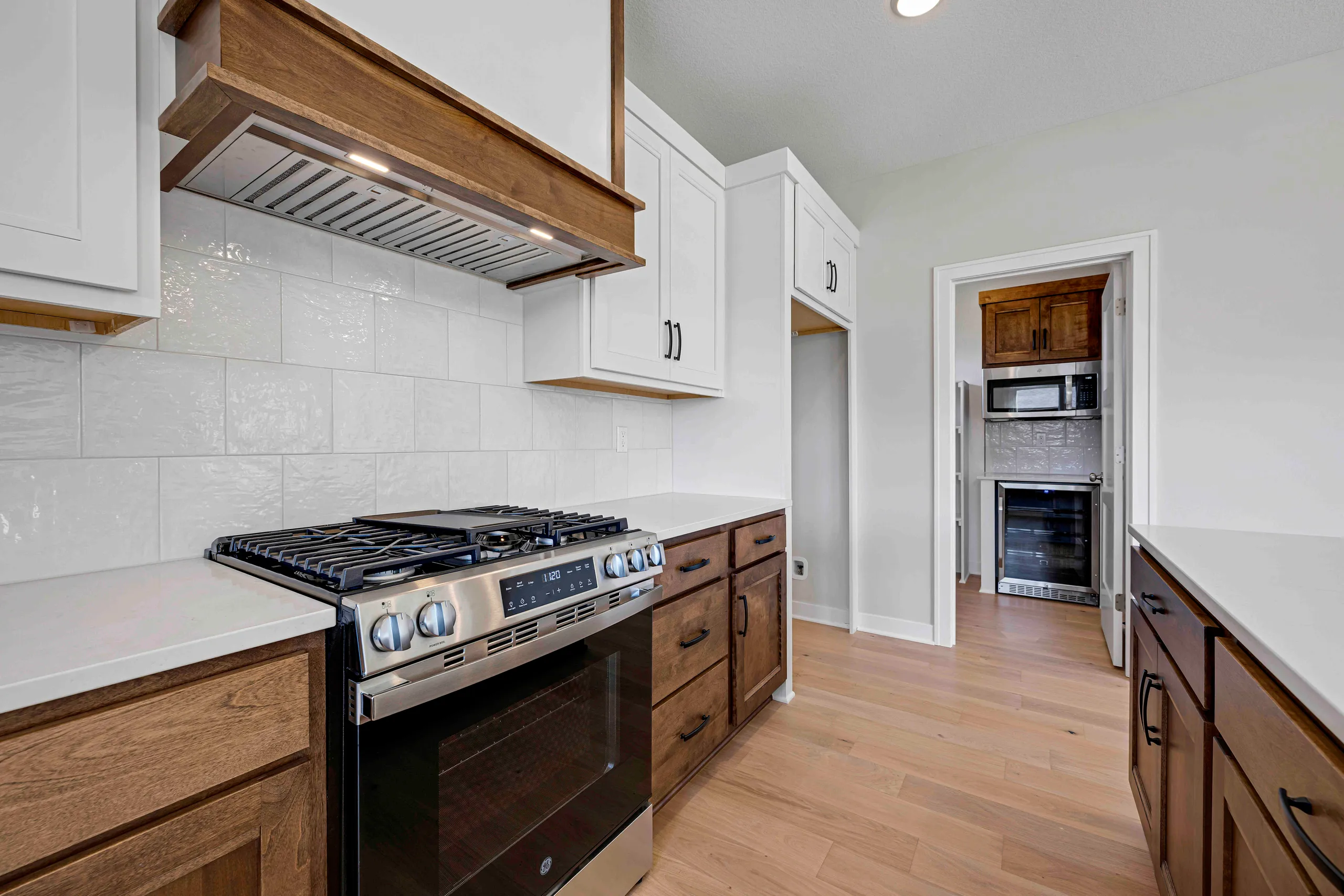 Kitchen with white subway tile backsplash, wood and white cabinetry, stainless steel gas range, and wood flooring.