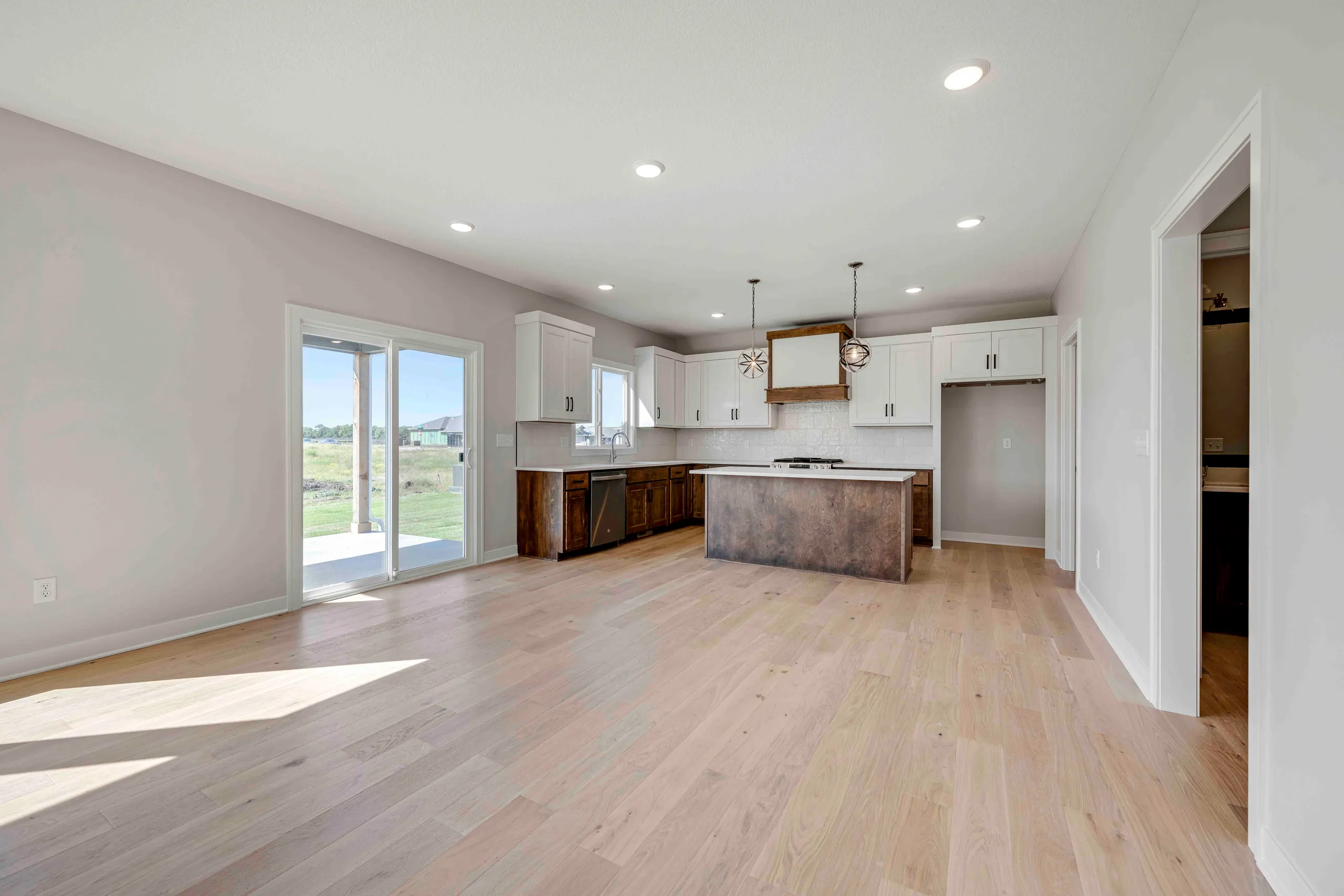 Open kitchen and dining area with white cabinets, wood island, glass doors leading to patio, and hardwood flooring.