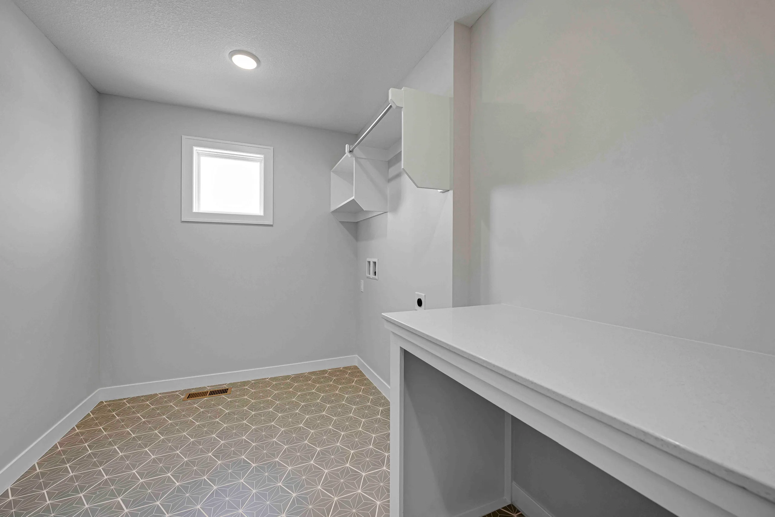 Laundry room with white walls, geometric tile flooring, white countertop, wall-mounted shelving, and small window.