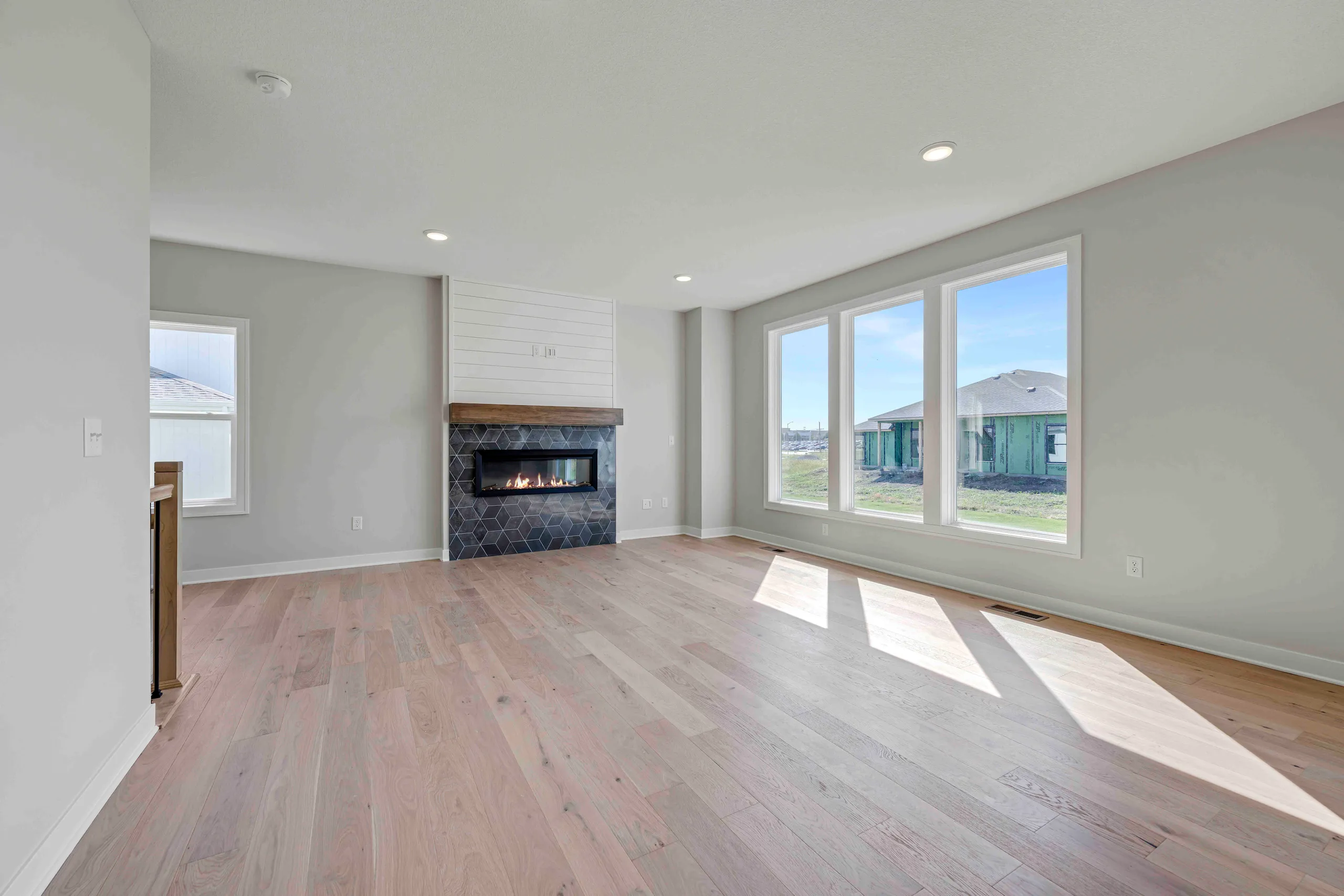 Open living room with wood flooring, fireplace with dark tile surround, and large windows overlooking neighborhood.