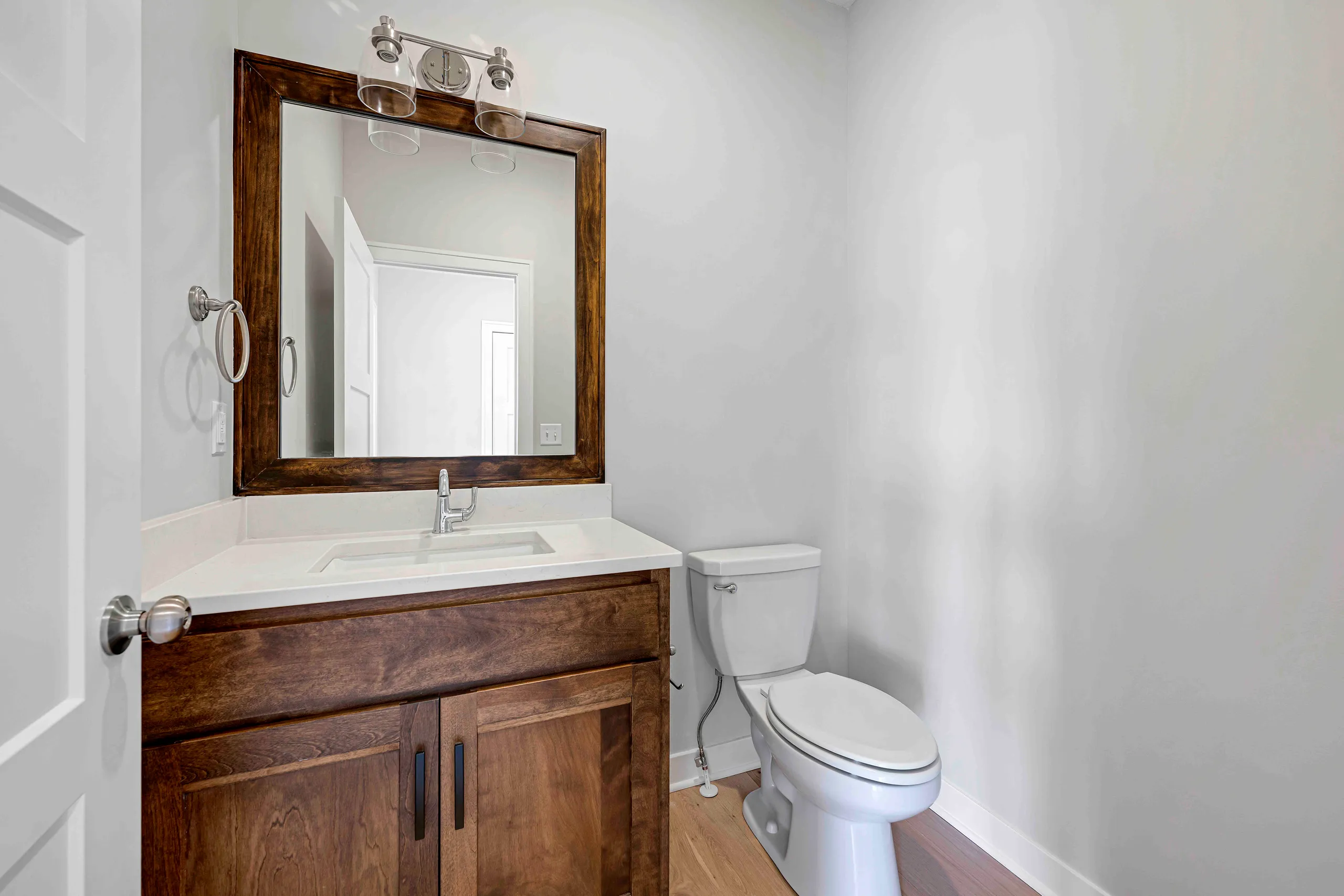 Bathroom with wood vanity, white sink, framed mirror with three-light fixture above, and white toilet.