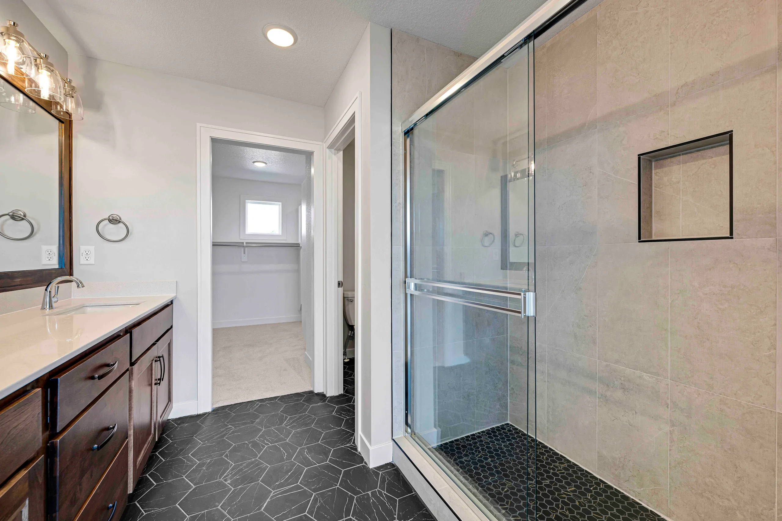 Bathroom with dark wood vanity, white quartz countertop, glass shower enclosure with tile surround, and hexagonal floor