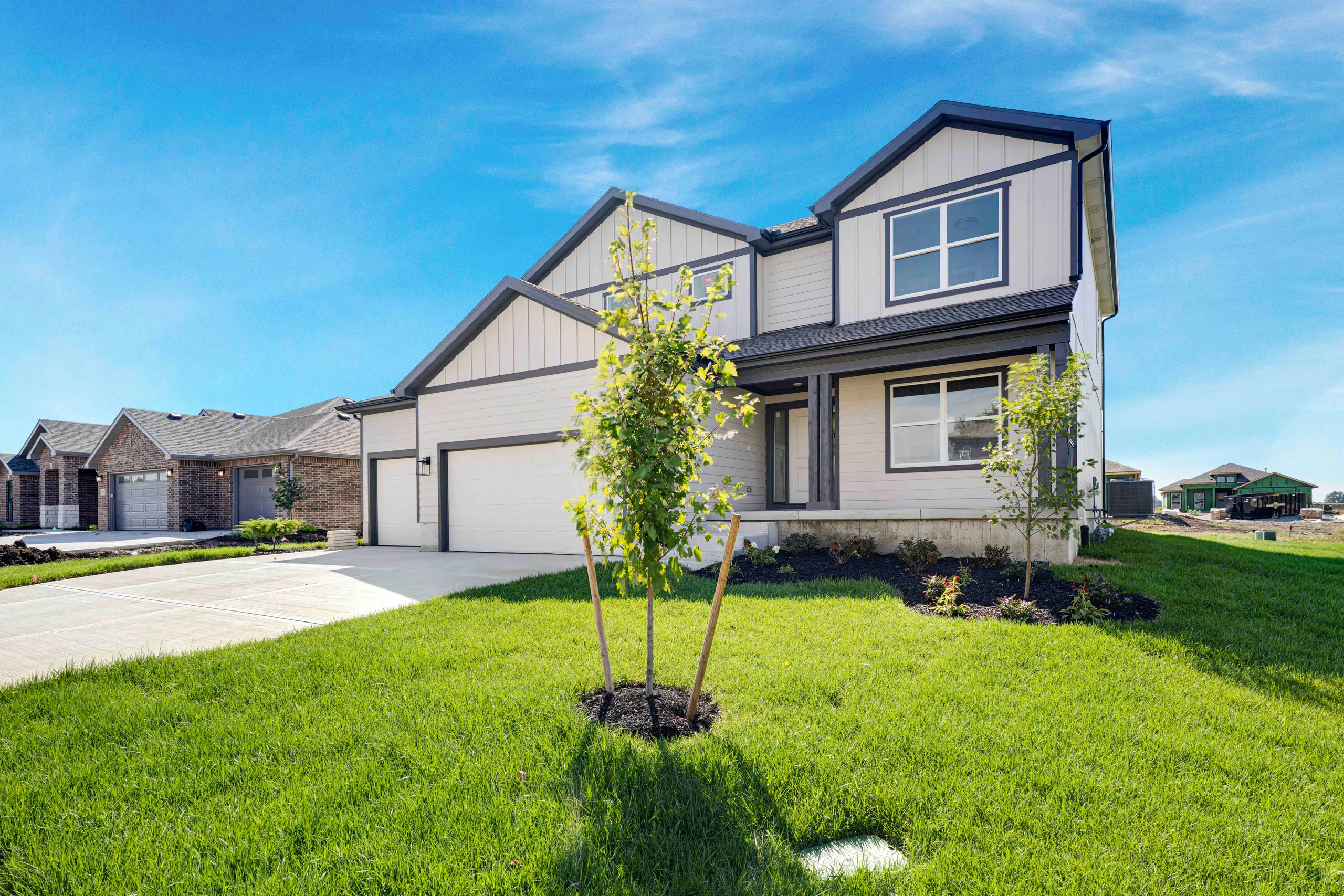Two-story home with white siding and dark trim featuring a two-car garage and young tree in front yard.