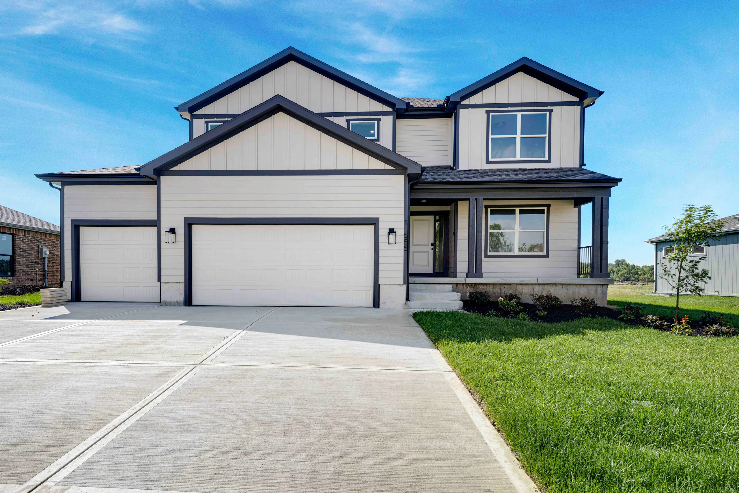 Two-story white and dark blue home with three-car garage, front porch, and landscaped lawn.