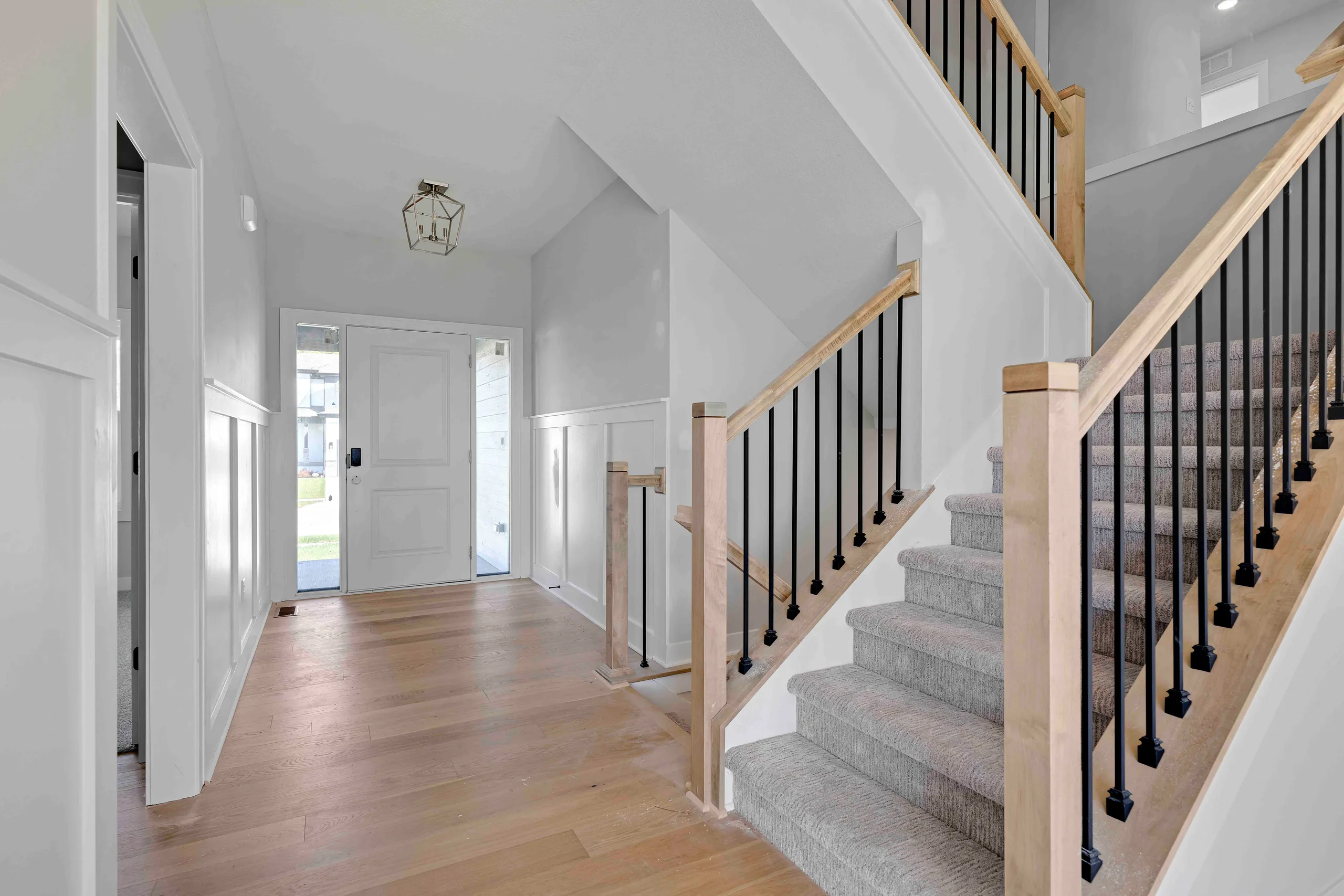Foyer with white walls, wood flooring, staircase with wood handrail and black spindles, and front door with sidelights.