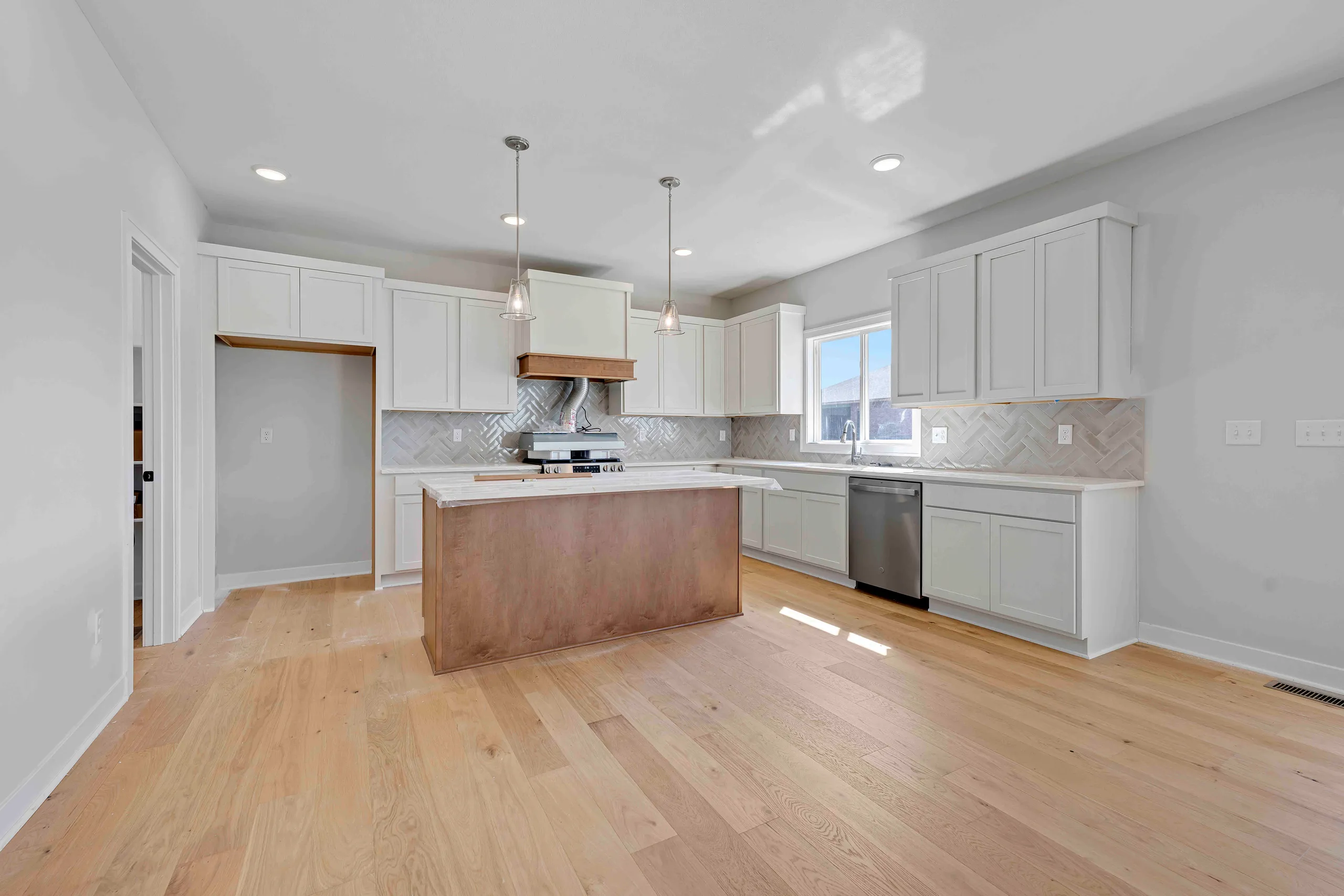 Kitchen with white cabinetry, wood island, stainless steel appliances, herringbone backsplash, and hardwood flooring.