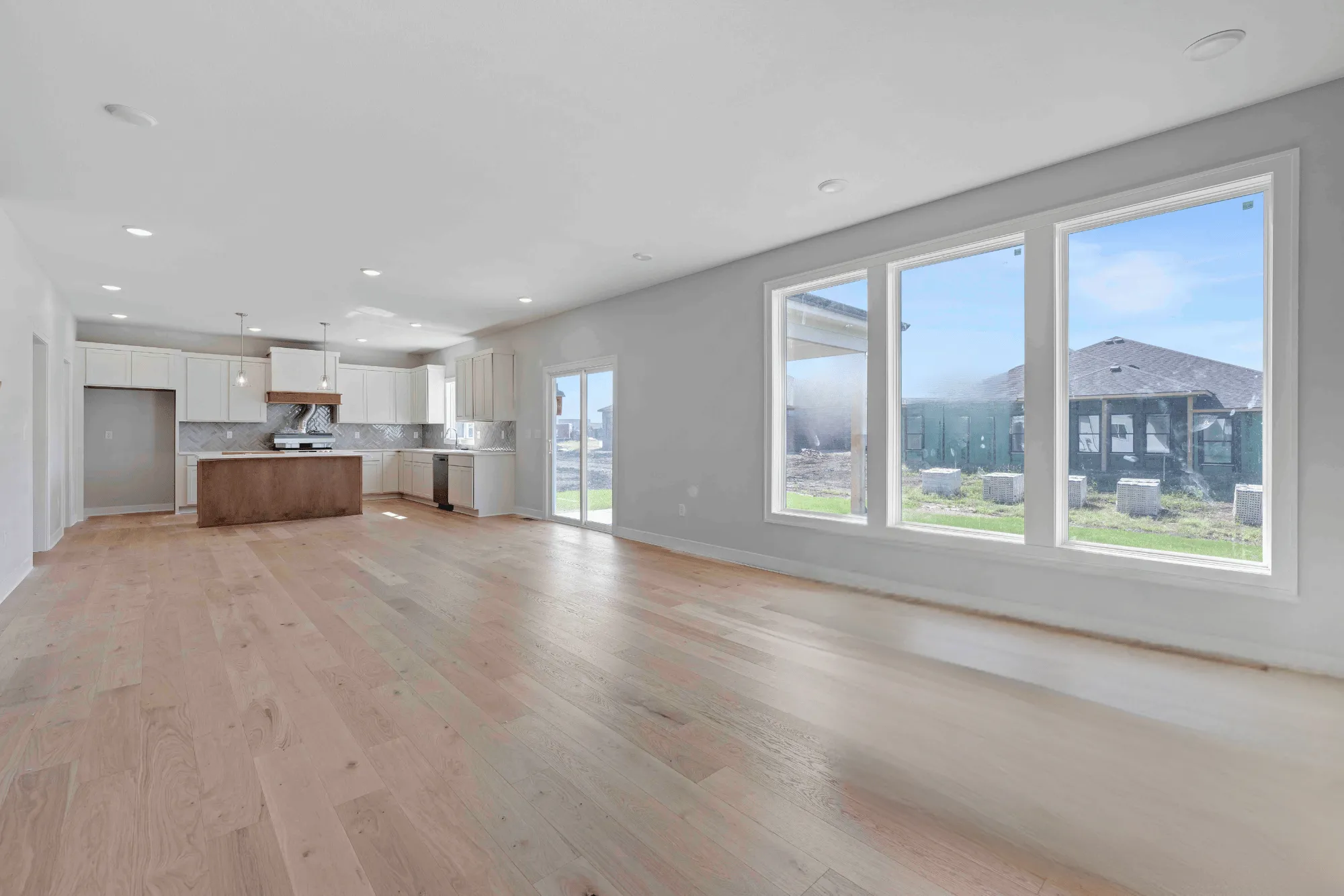 Open-concept living area with wood flooring, white kitchen cabinetry, brown island, and large windows overlooking landscaped