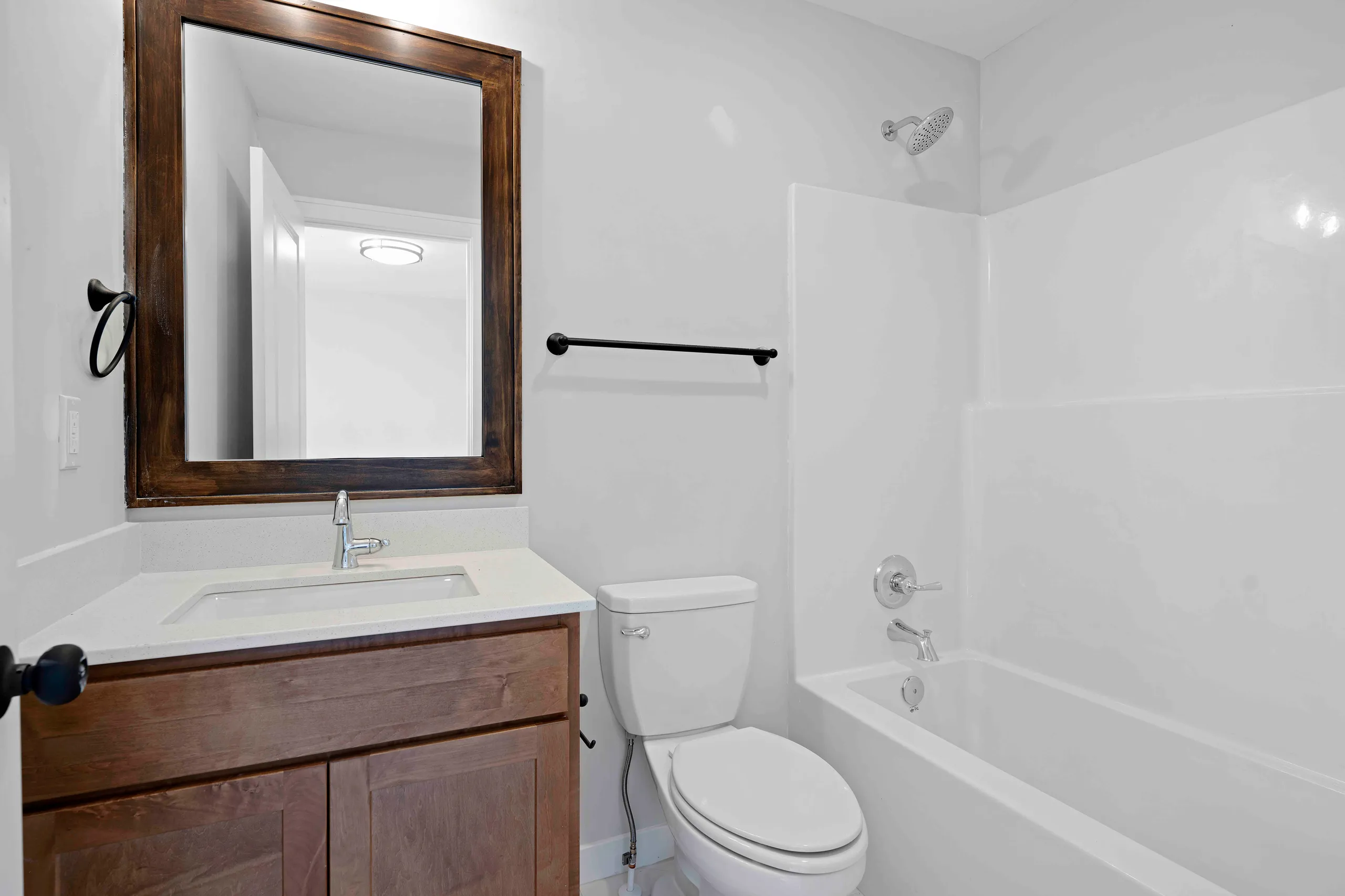 Bathroom with white subway tile walls, wood vanity with framed mirror, toilet, bathtub with shower enclosure and black