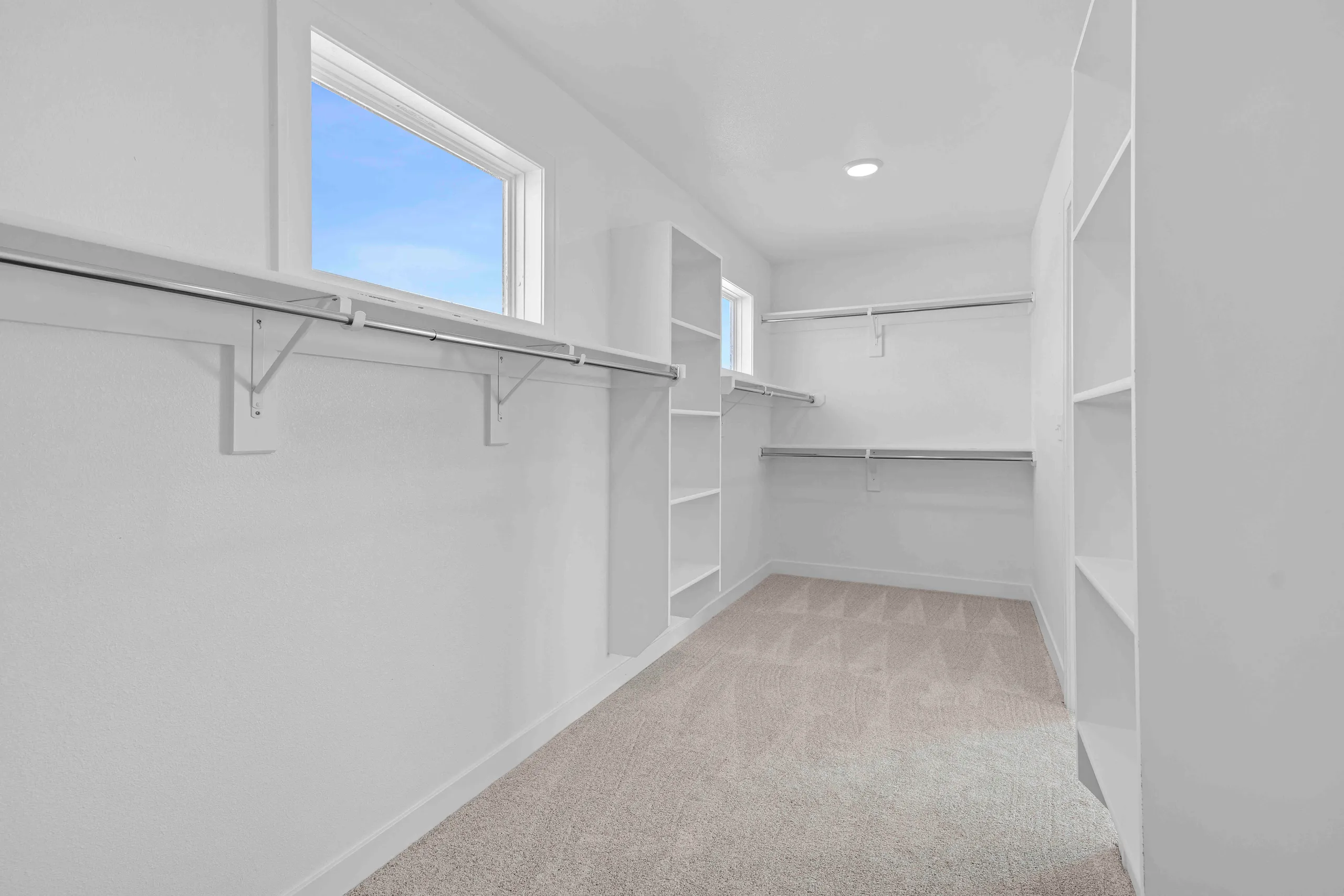Walk-in closet with white walls, built-in shelving and hanging rods, and a window with blue sky view.