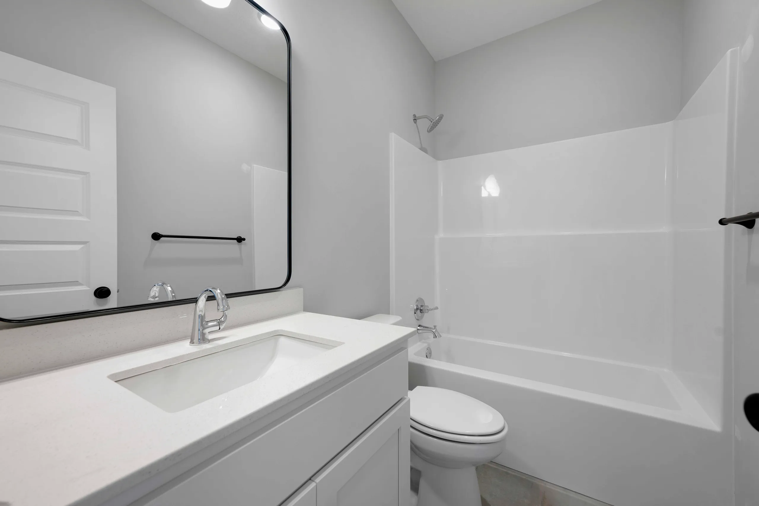 Bathroom with white vanity, undermount sink, mirror with black frame, toilet, and white tile shower surround.