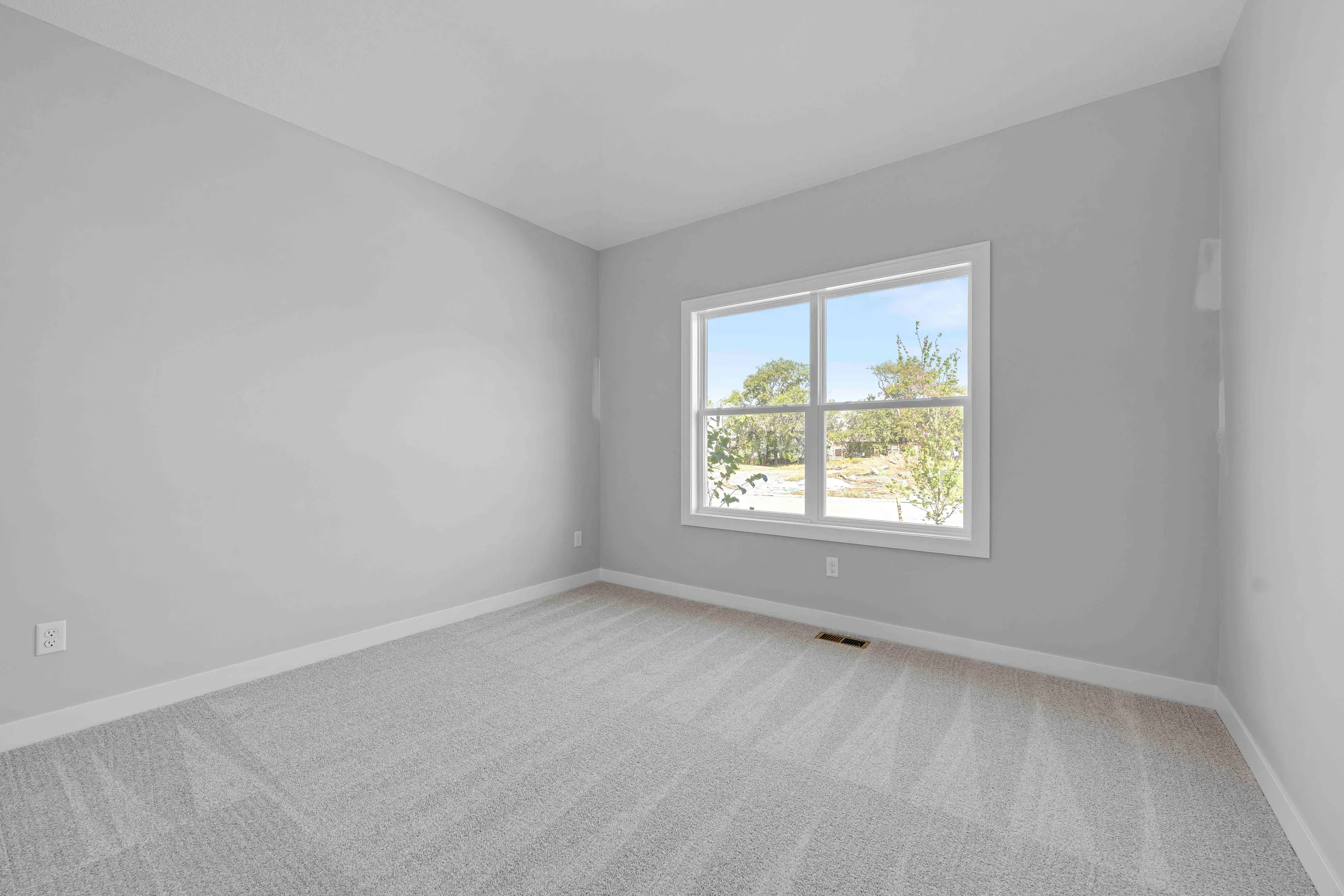Empty bedroom with gray walls, beige carpet, and large window overlooking trees and landscape.