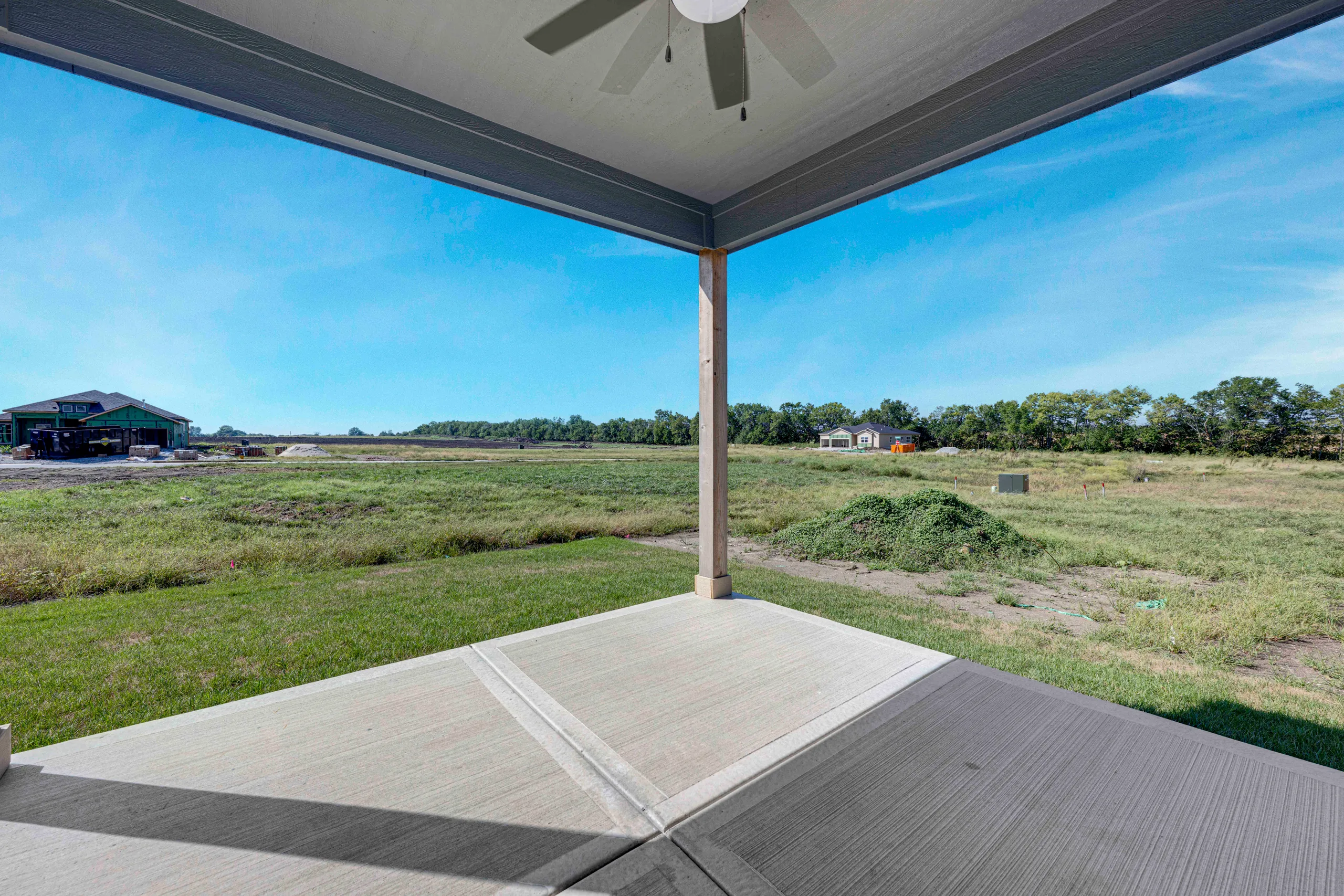 Covered patio with composite deck overlooking open rural landscape with distant buildings and tree line.