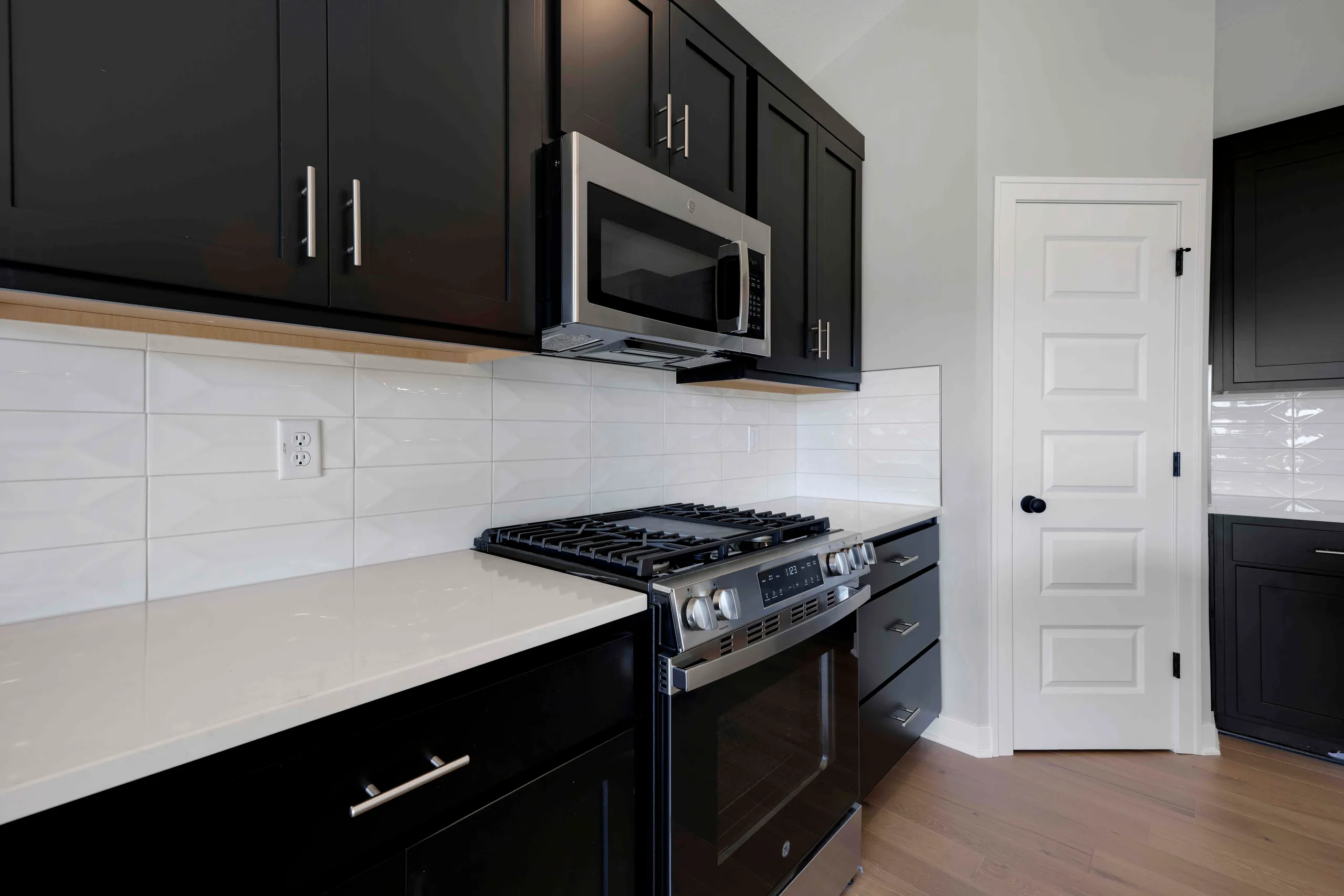 Black cabinetry with stainless steel gas range and microwave, white subway tile backsplash, and light countertop in modern