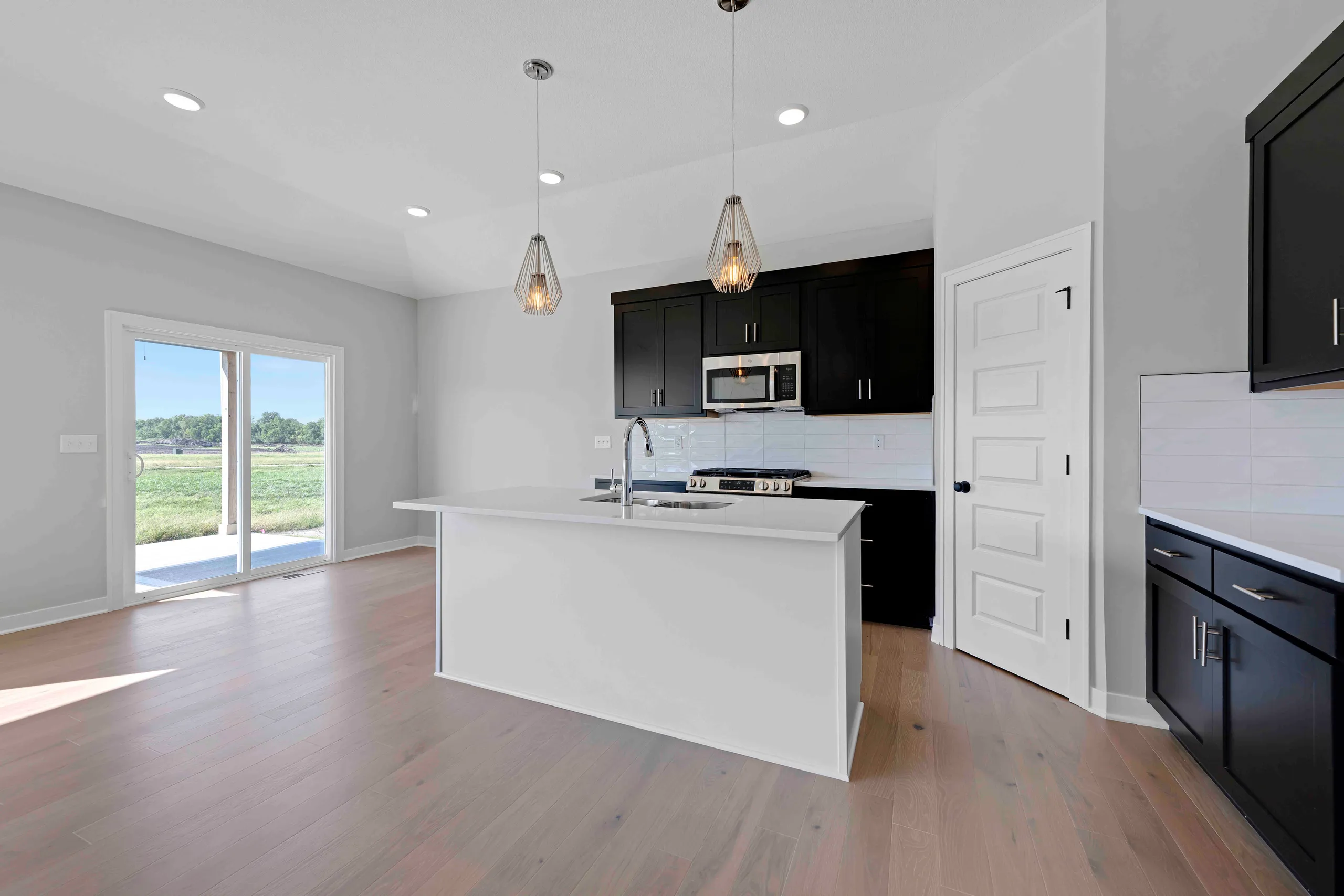 Kitchen with white island, black cabinetry, stainless steel appliances, pendant lights, and view of open field through glass