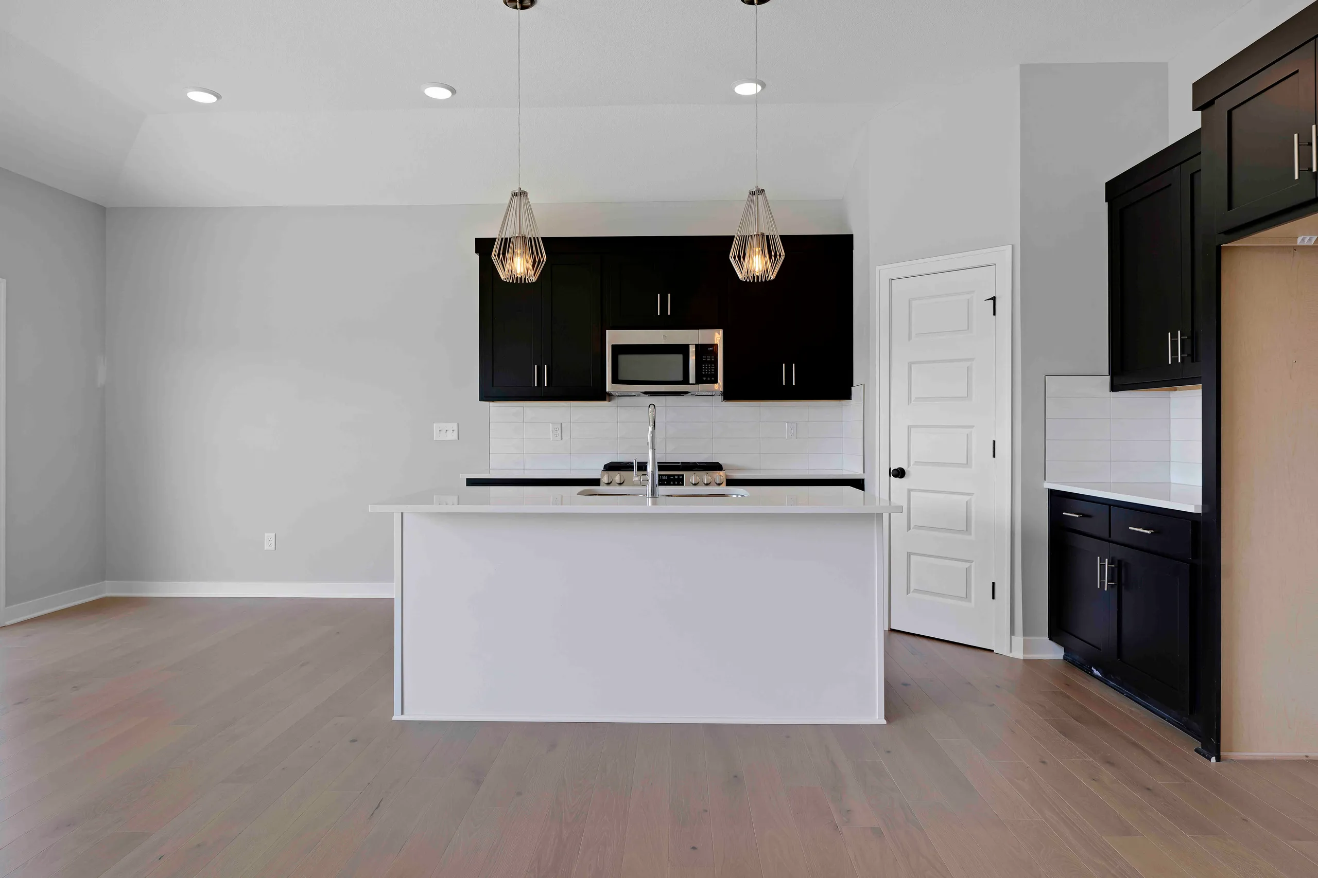 Kitchen with white island, black upper cabinets, white subway tile backsplash, pendant lights, and hardwood floors.