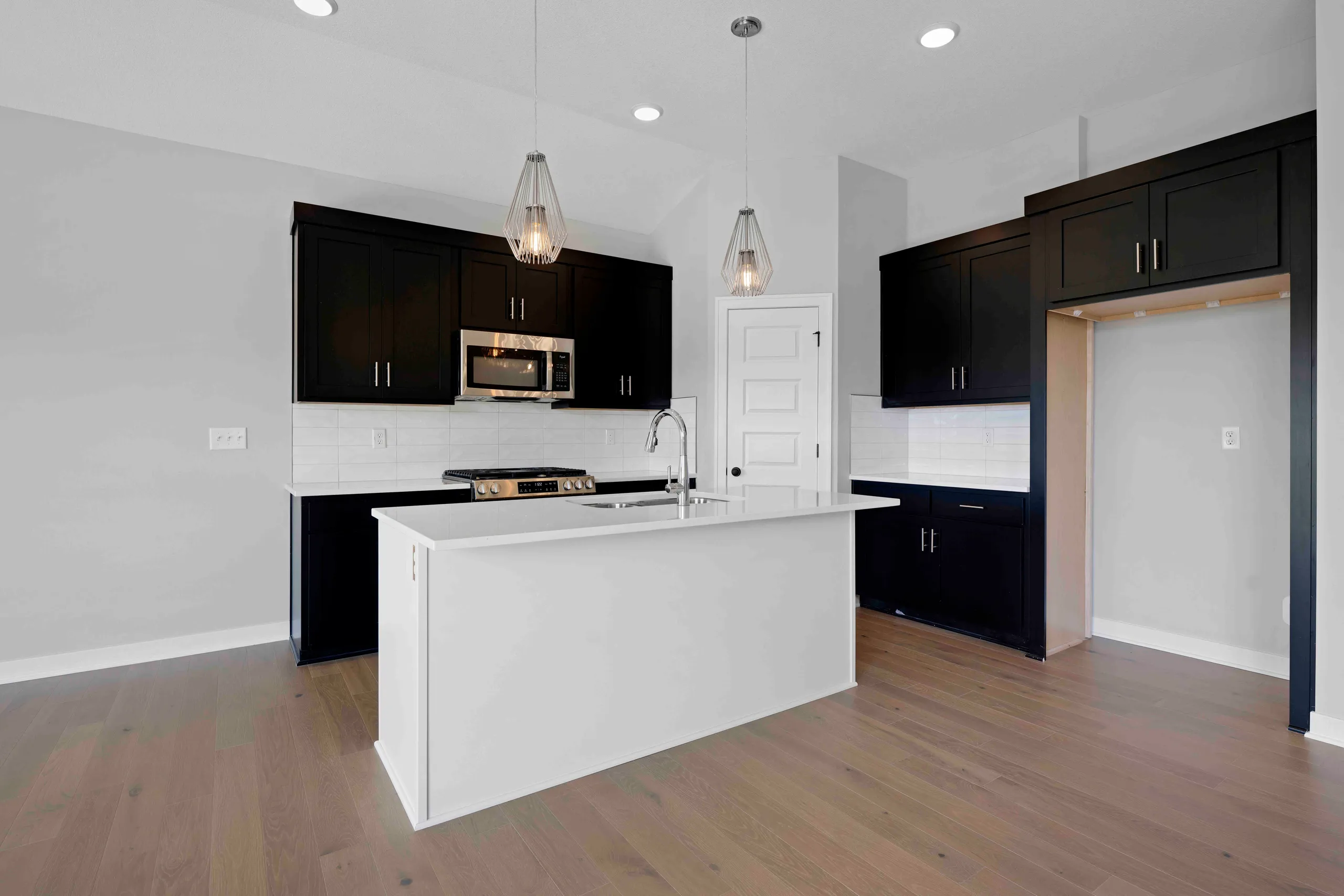 Kitchen with black cabinetry, white island, stainless steel appliances, white subway tile backsplash, and wood flooring.