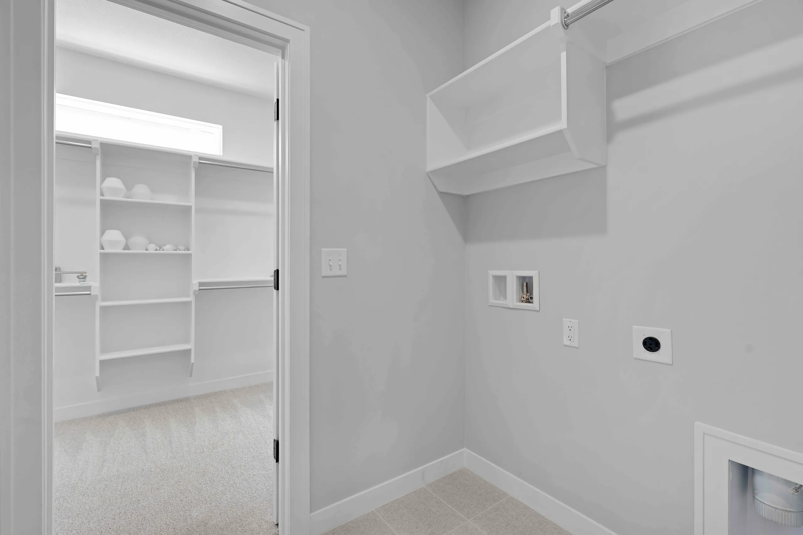 Laundry room with tile flooring, white walls, open shelving visible through doorway, and dryer vent on wall.