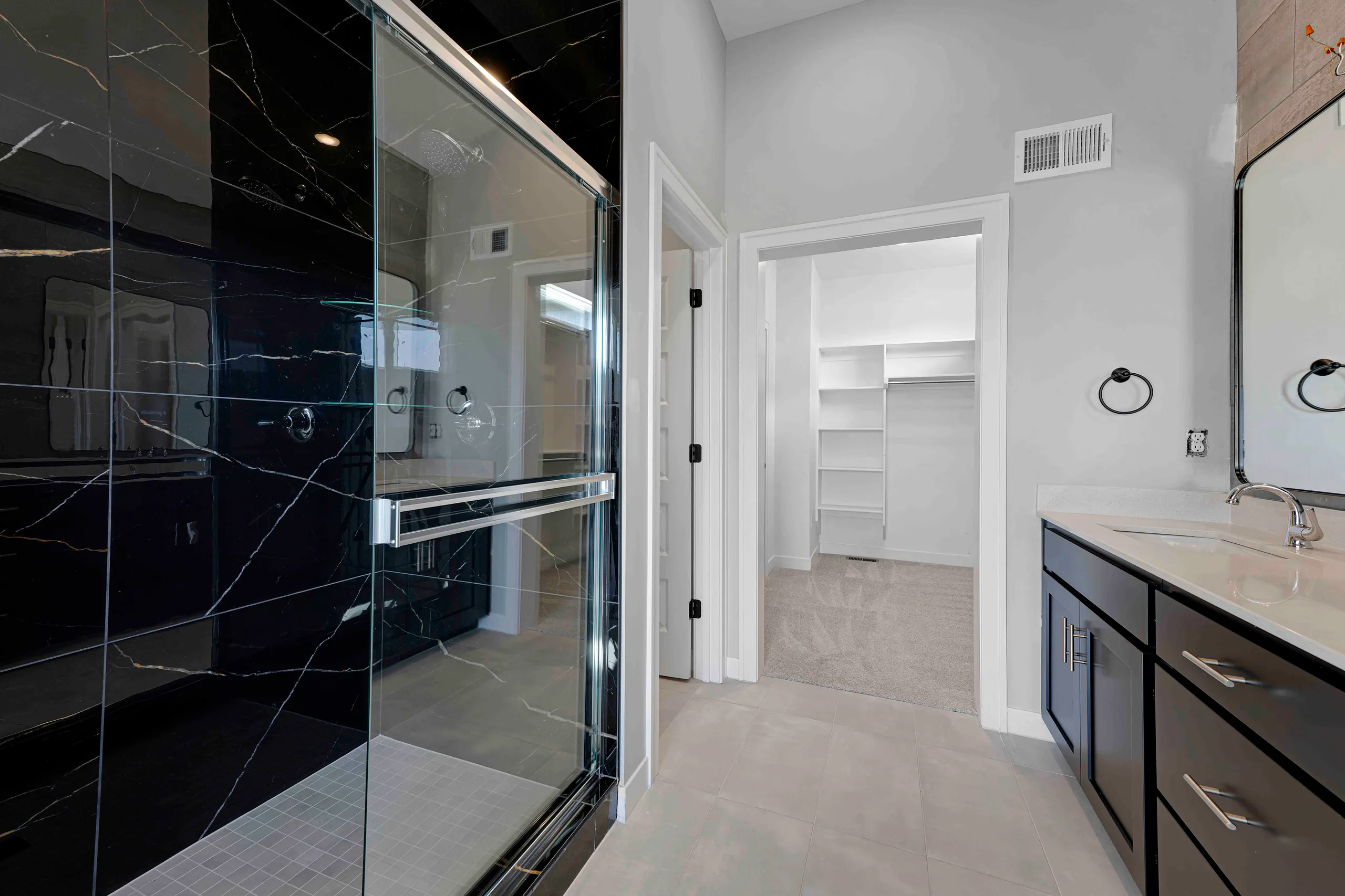 Master bathroom with black marble walk-in shower, double vanity with dark cabinetry, and walk-in closet.