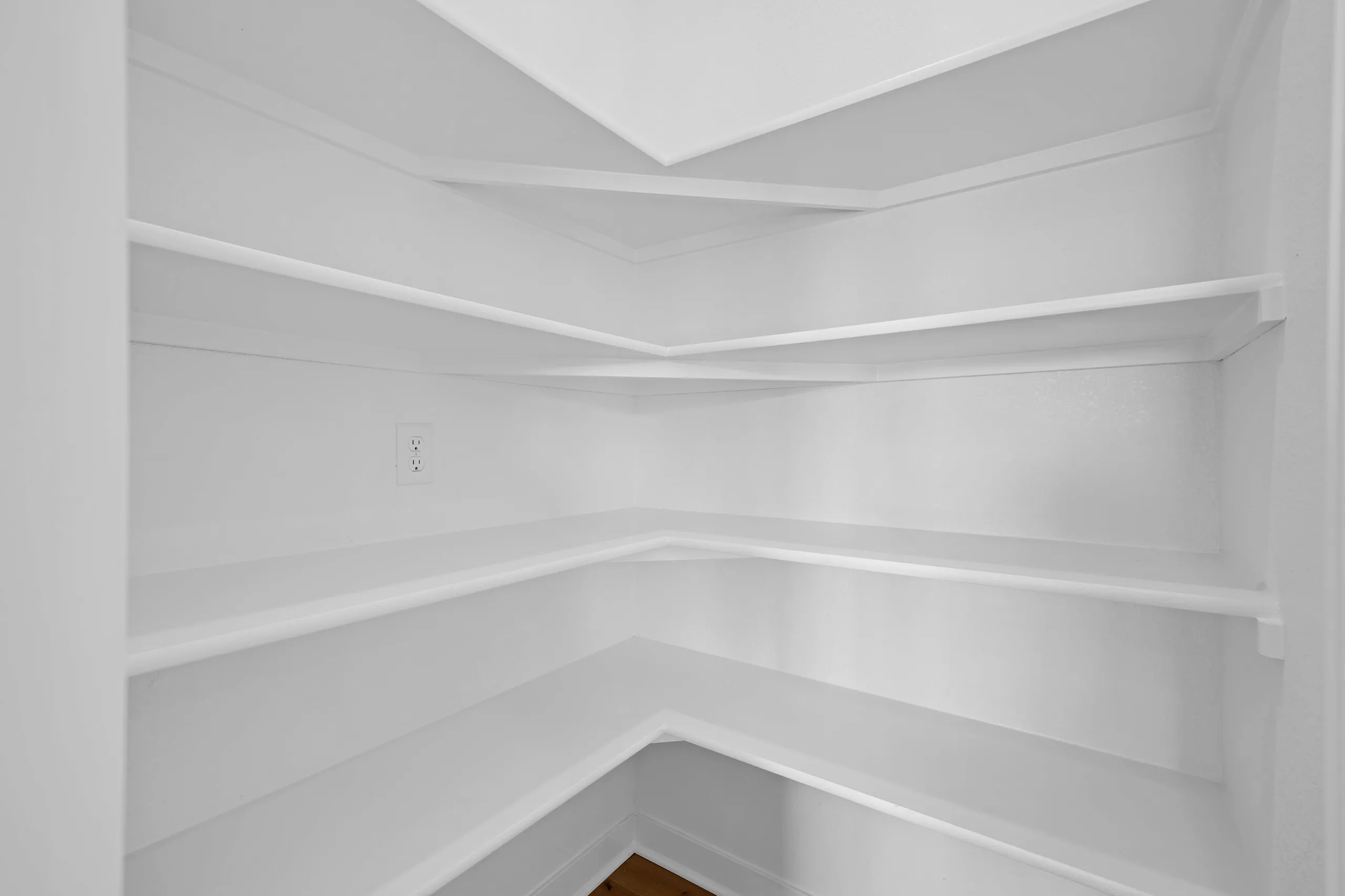 Empty white shelving closet with curved corner shelves and recessed ceiling light.