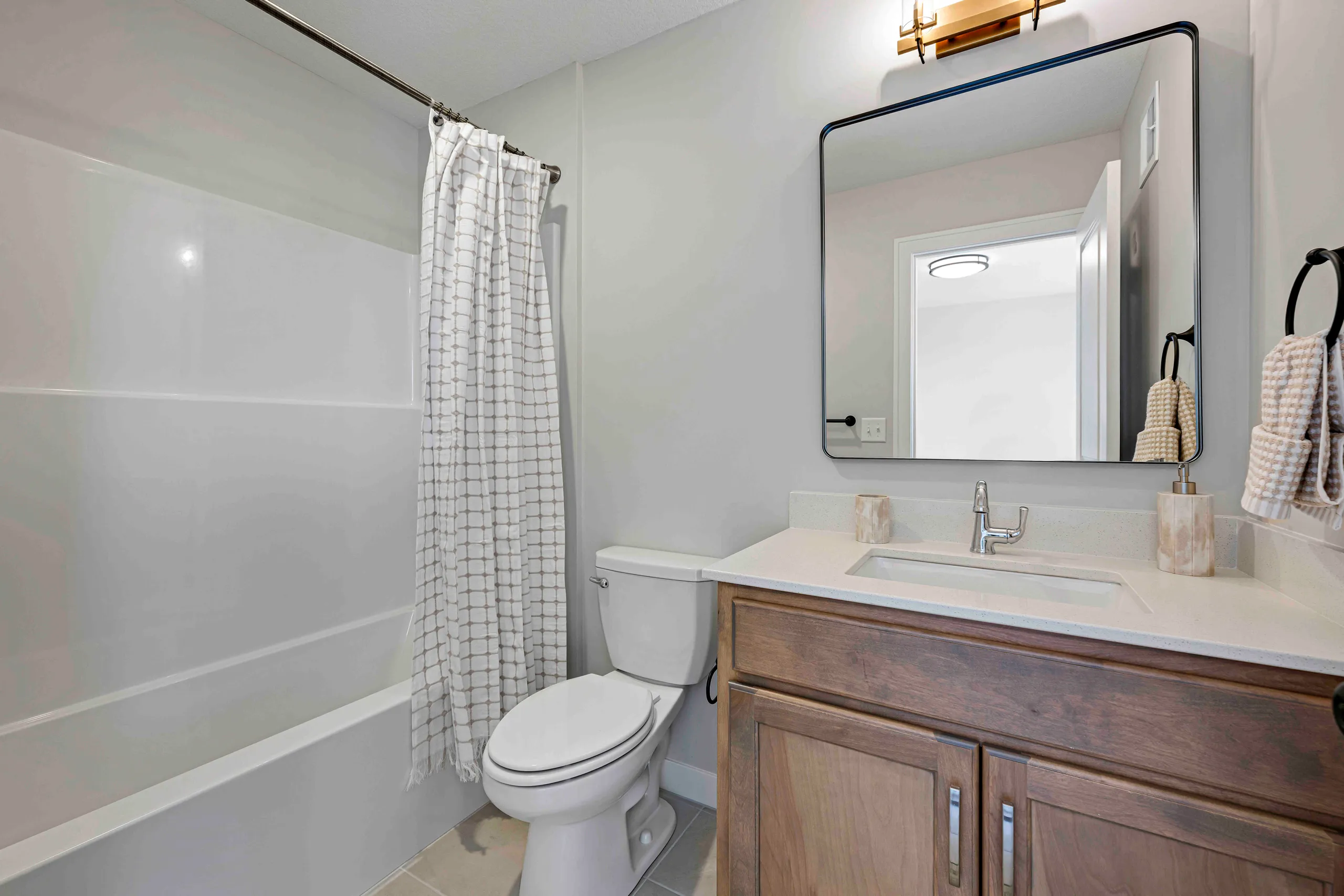 Bathroom with white subway tile walls, wooden vanity with sink, framed mirror, toilet, and shower with checkered curtain.