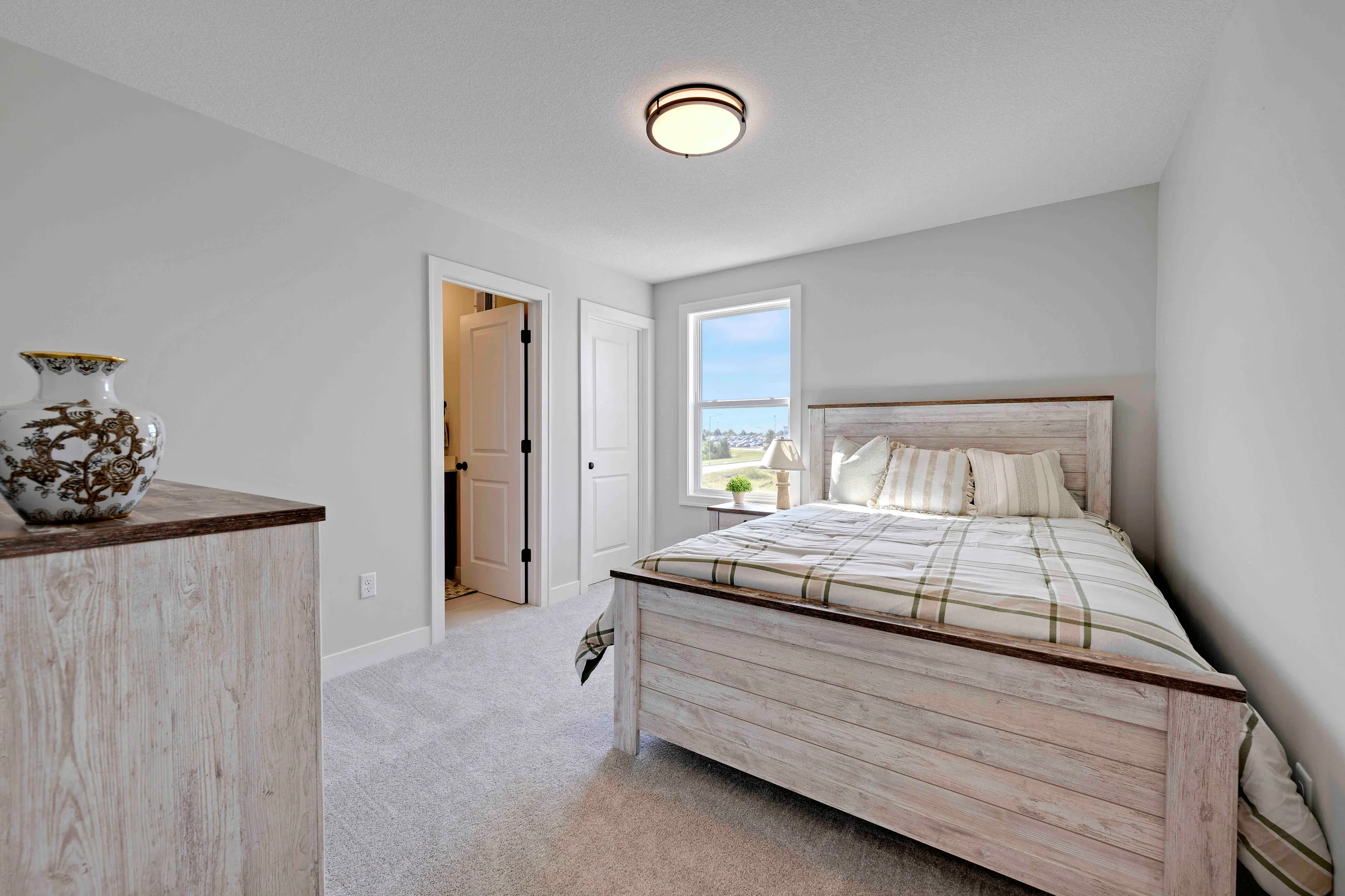 Bedroom with light wood bed frame, striped bedding, window with water view, dresser with decorative vase, and ceiling light