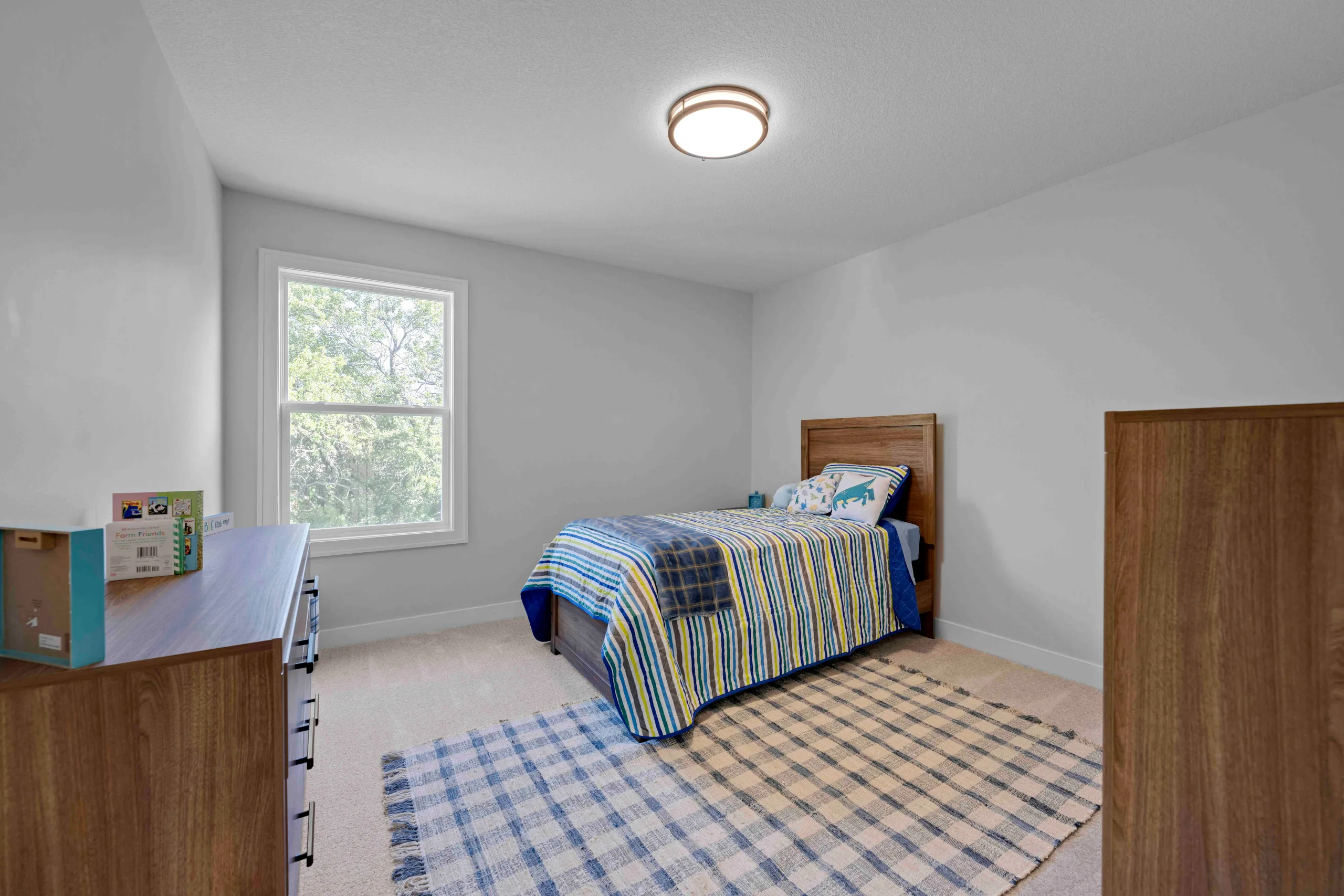 Child's bedroom with wooden bed frame, blue striped bedding, large window, wood dresser, and ceiling light fixture.