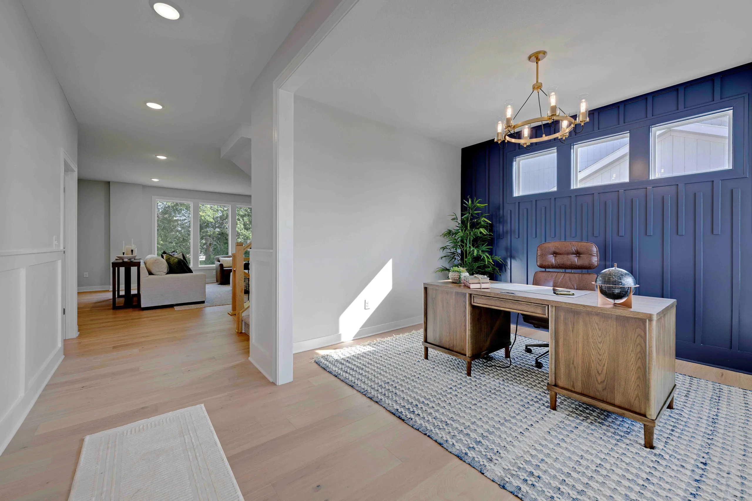 Home office with wood desk, brown leather chair, navy blue built-in cabinets, and view into adjoining living room with