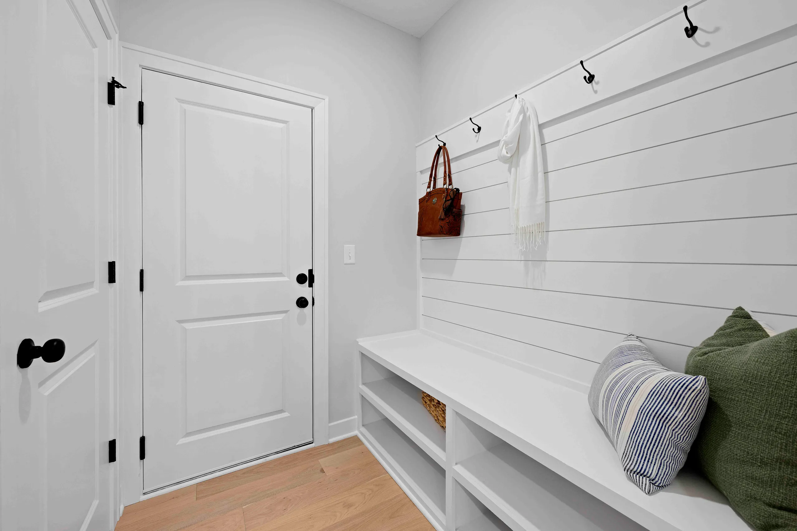 White mudroom with built-in bench, shiplap walls, black hardware, and white door with black handles.