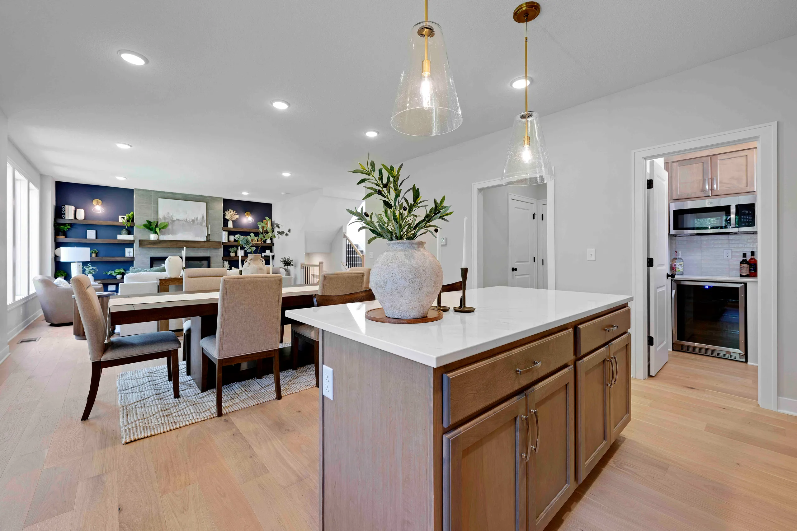 Open kitchen and dining area with wood cabinetry island, white countertops, pendant lighting, and view into living room with