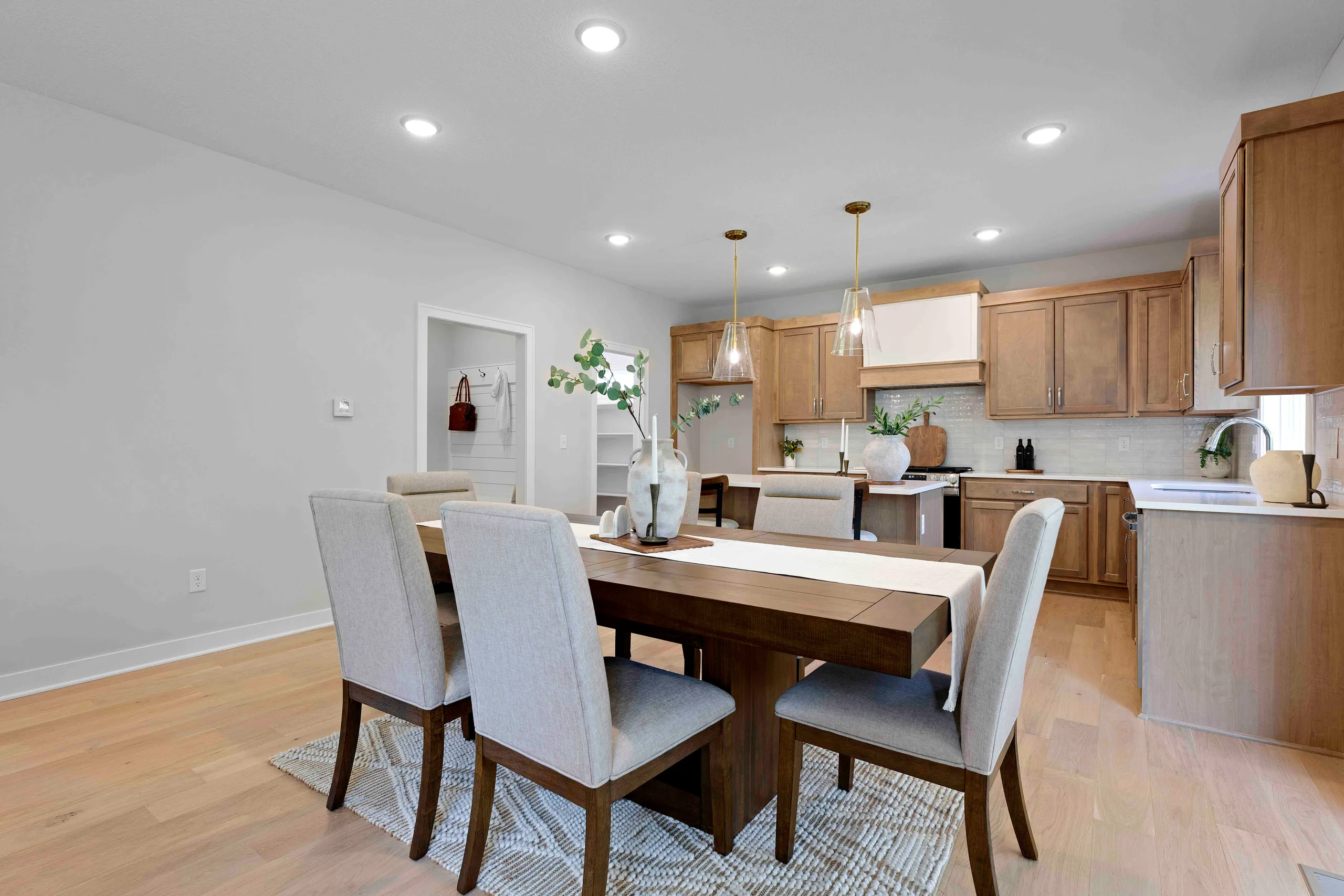 Dining and kitchen area with wooden table, upholstered chairs, wood cabinetry, and recessed lighting.