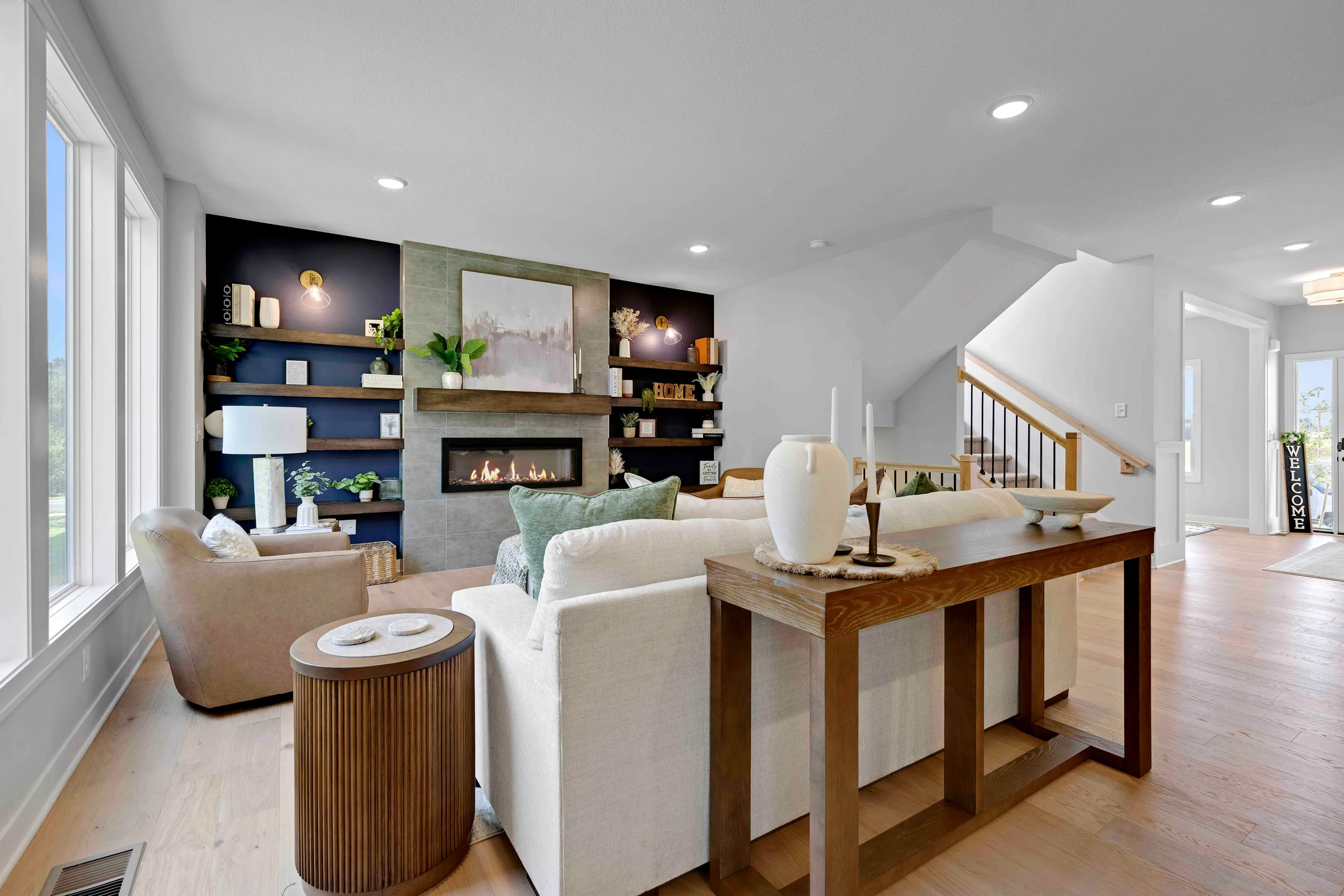 Living room with cream seating, wood console table, fireplace with dark shelving, and stairs to upper level.