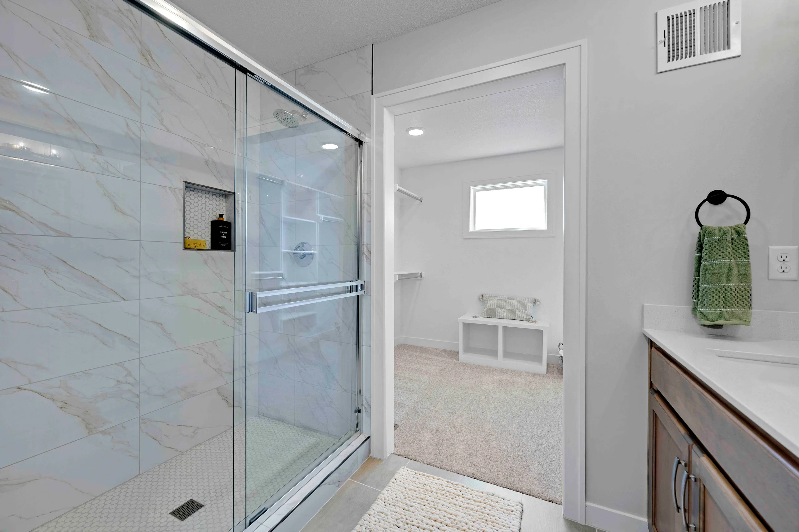Bathroom with marble tile shower enclosure, white vanity with wood cabinetry, and doorway to bedroom.