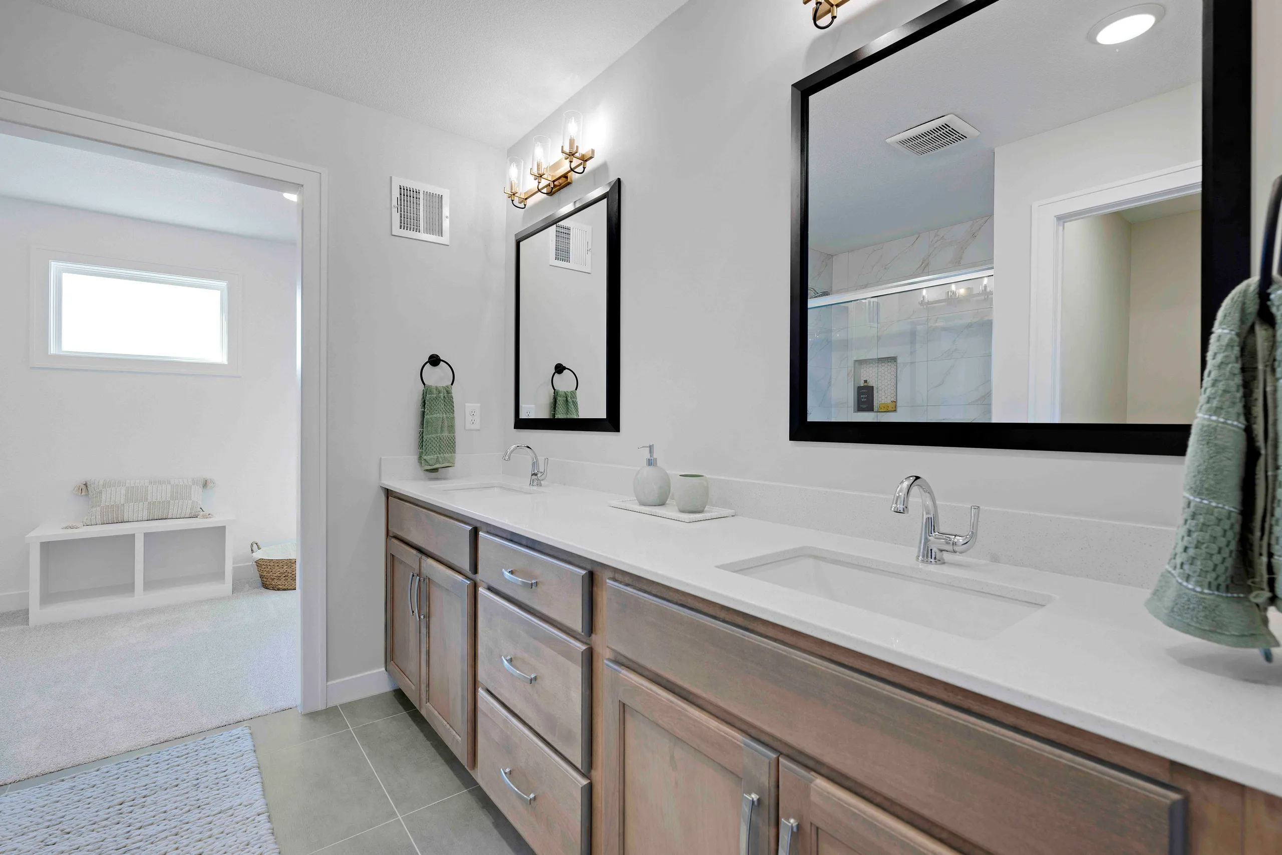 Bathroom with double vanity, white countertop, wood cabinetry, black-framed mirrors, and doorway to bathtub area.