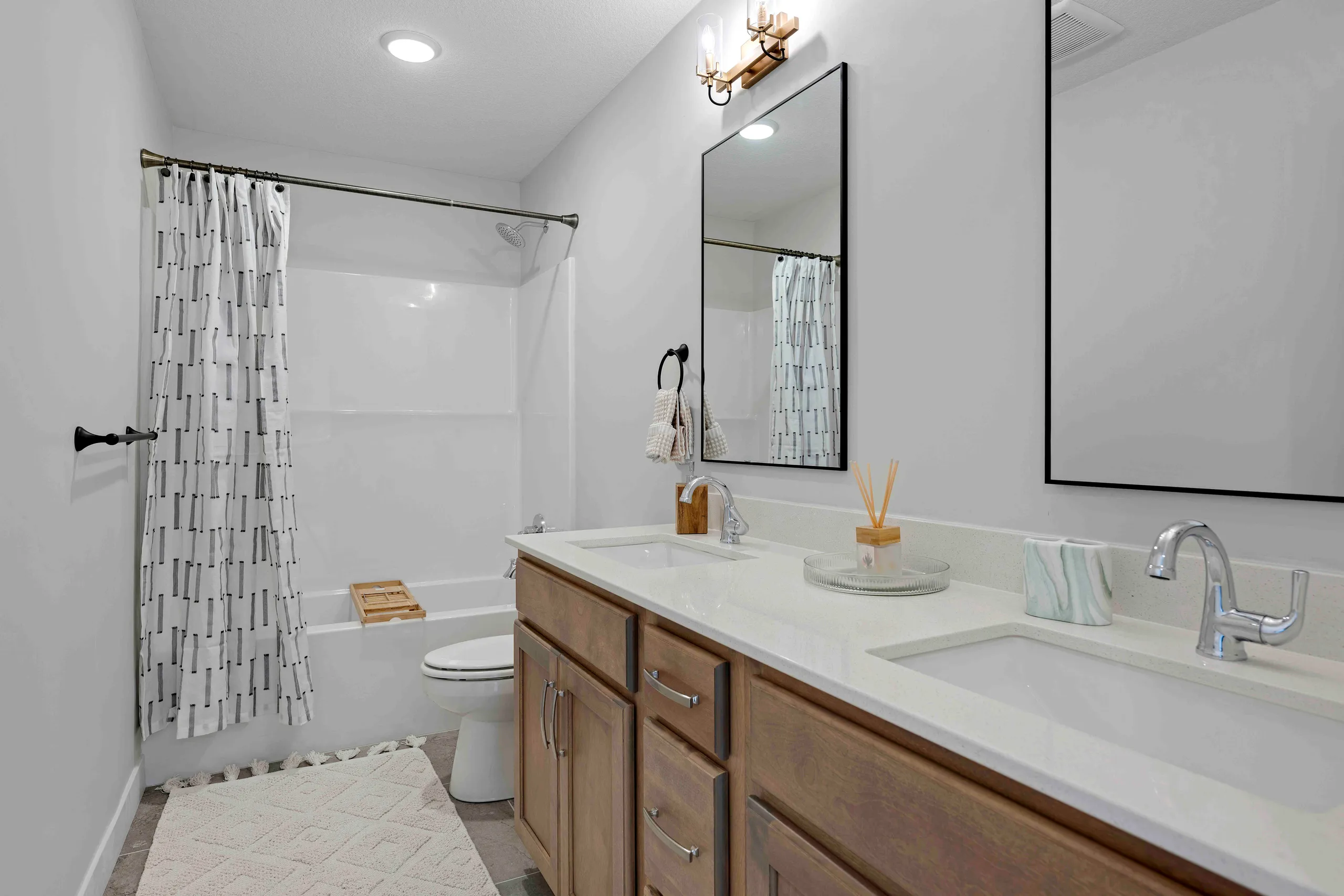 Bathroom with white walls, dual-sink vanity with wood cabinetry, white countertop, and shower with patterned curtain.