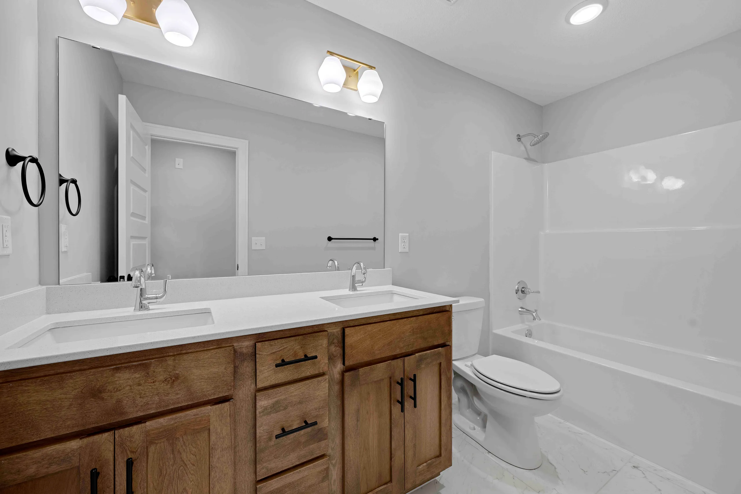 Bathroom with double vanity, wooden cabinets, white countertop, large mirror, toilet, and bathtub with tile surround.