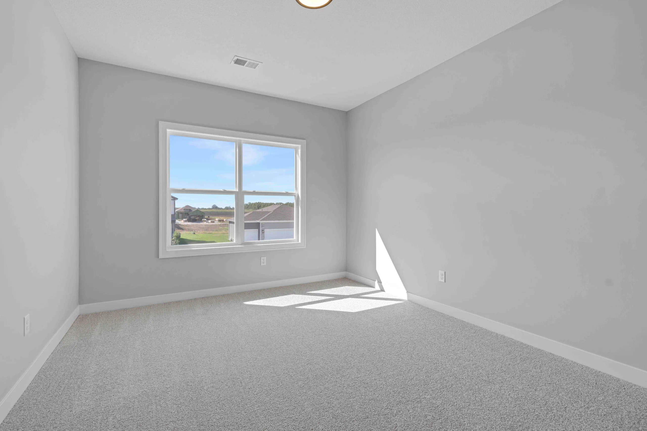 Empty bedroom with gray walls, gray carpet, and large window overlooking residential community.