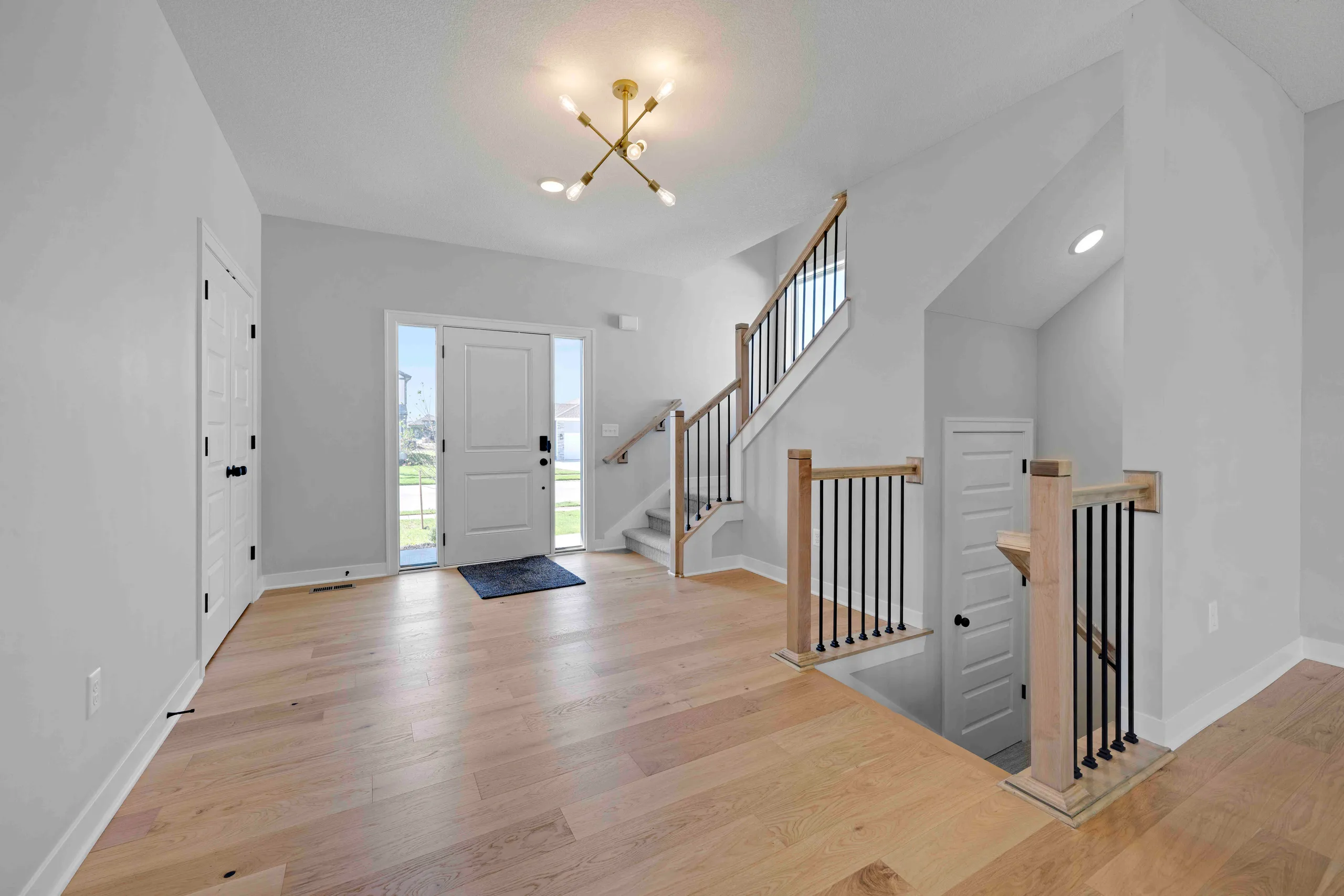 Two-story foyer with wooden staircase, white walls, wood flooring, and glass front door with exterior view.