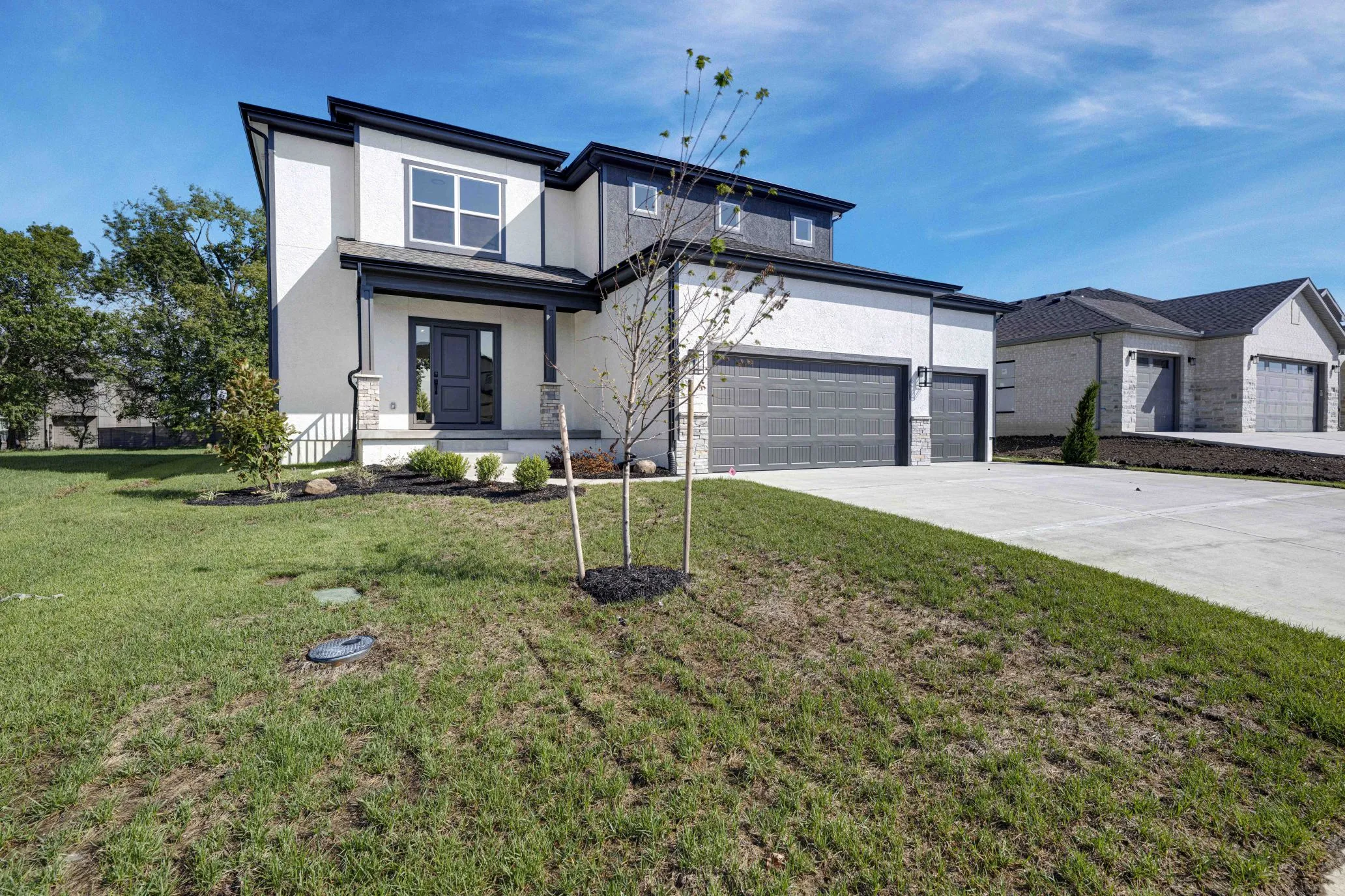 Two-story house with white and gray exterior, dark roof, front porch, and three-car garage on landscaped lot.