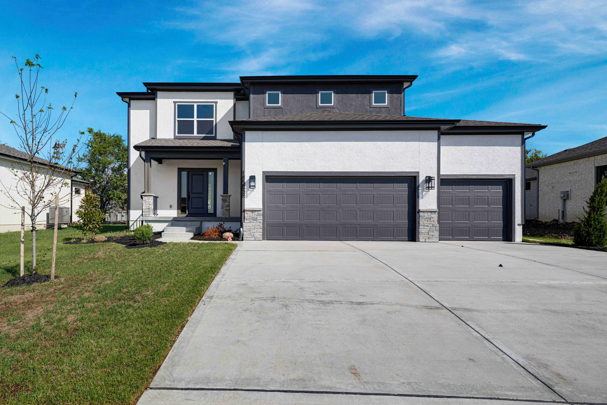 Two-story white and gray home with dark trim, two-car garage, and concrete driveway on landscaped lawn.