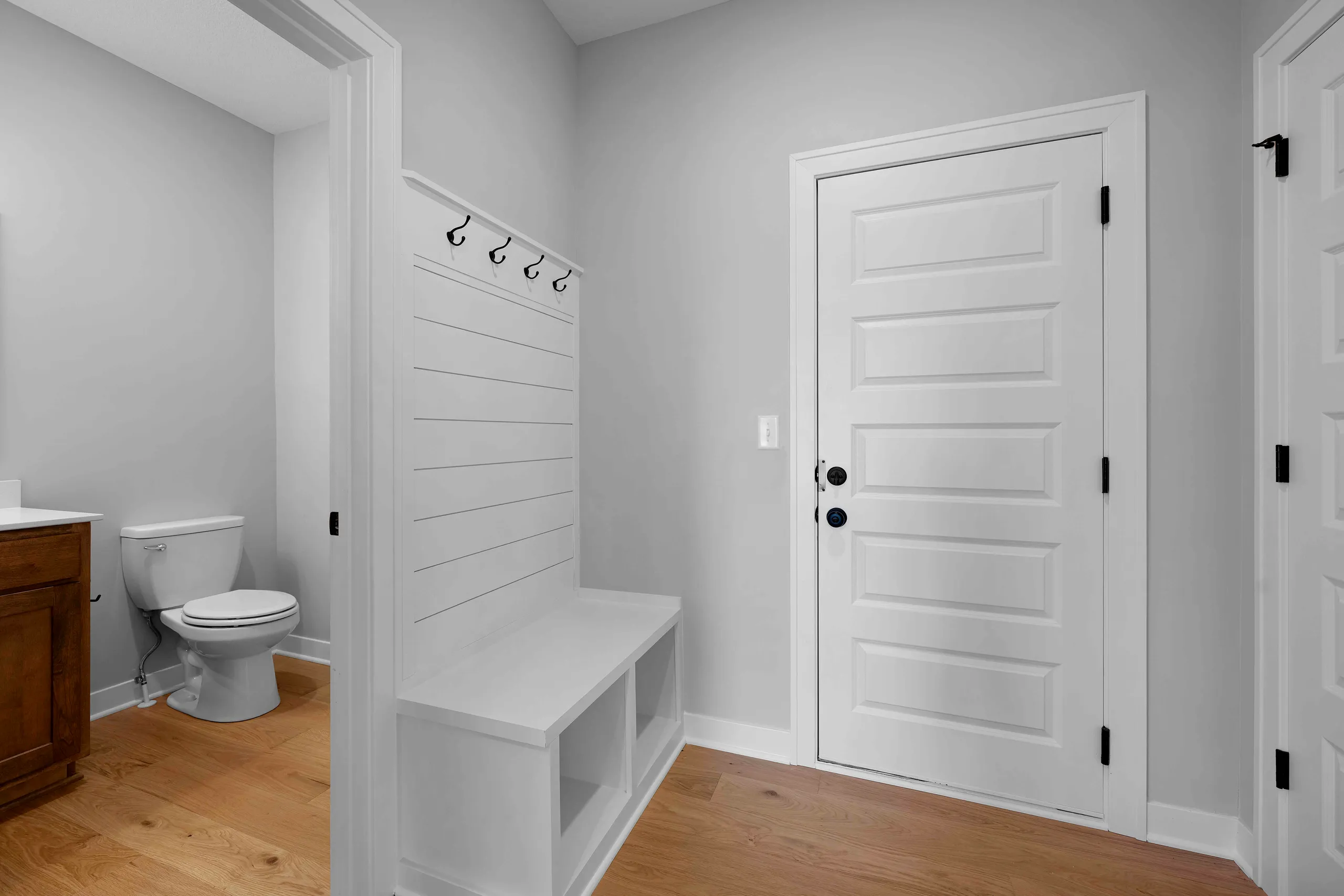 Mudroom with white shiplap walls, wooden bench with storage cubbies, coat hooks, and white paneled doors opening to bathroom