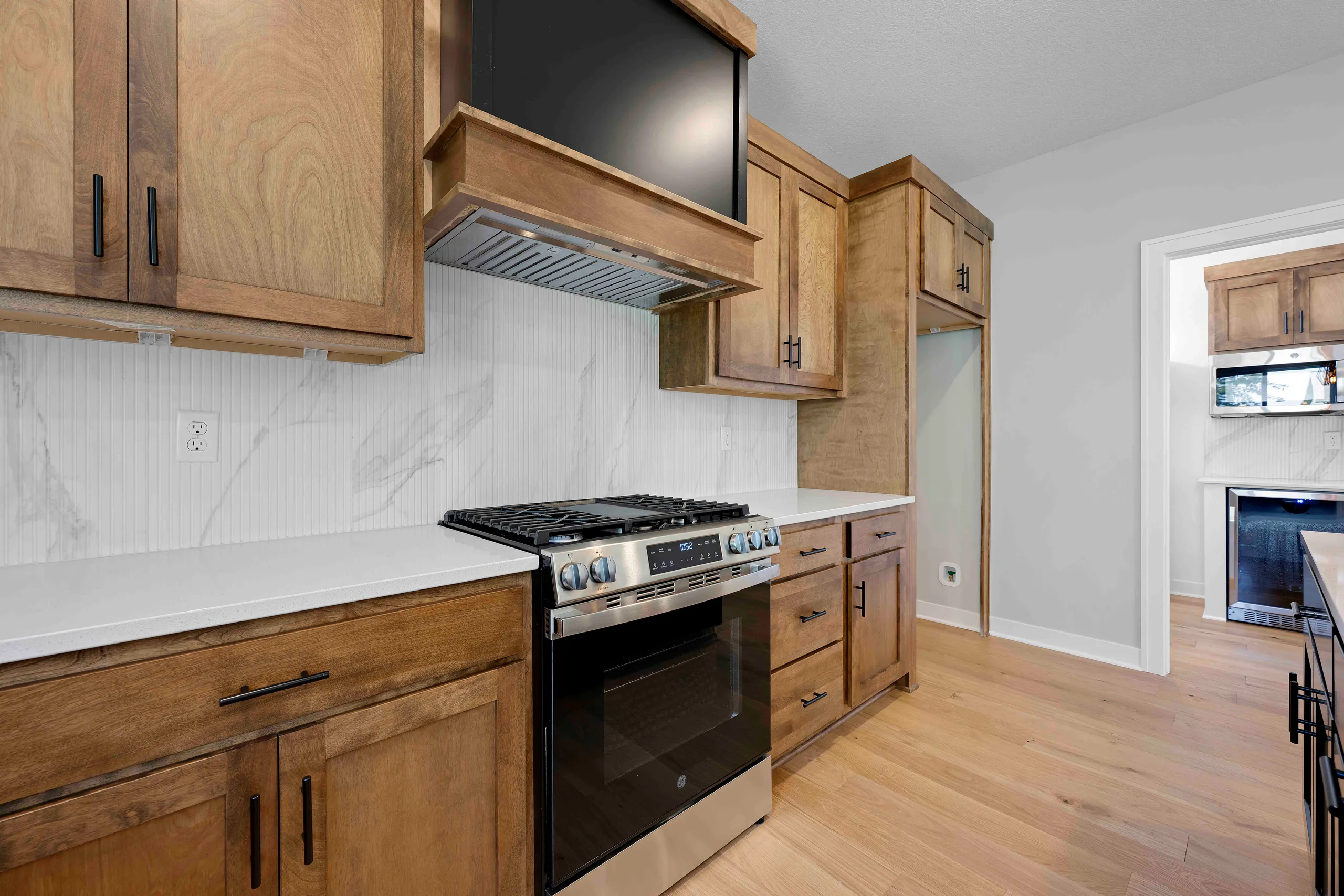 Kitchen with wooden cabinets, white marble backsplash, stainless steel gas range, and white countertops.