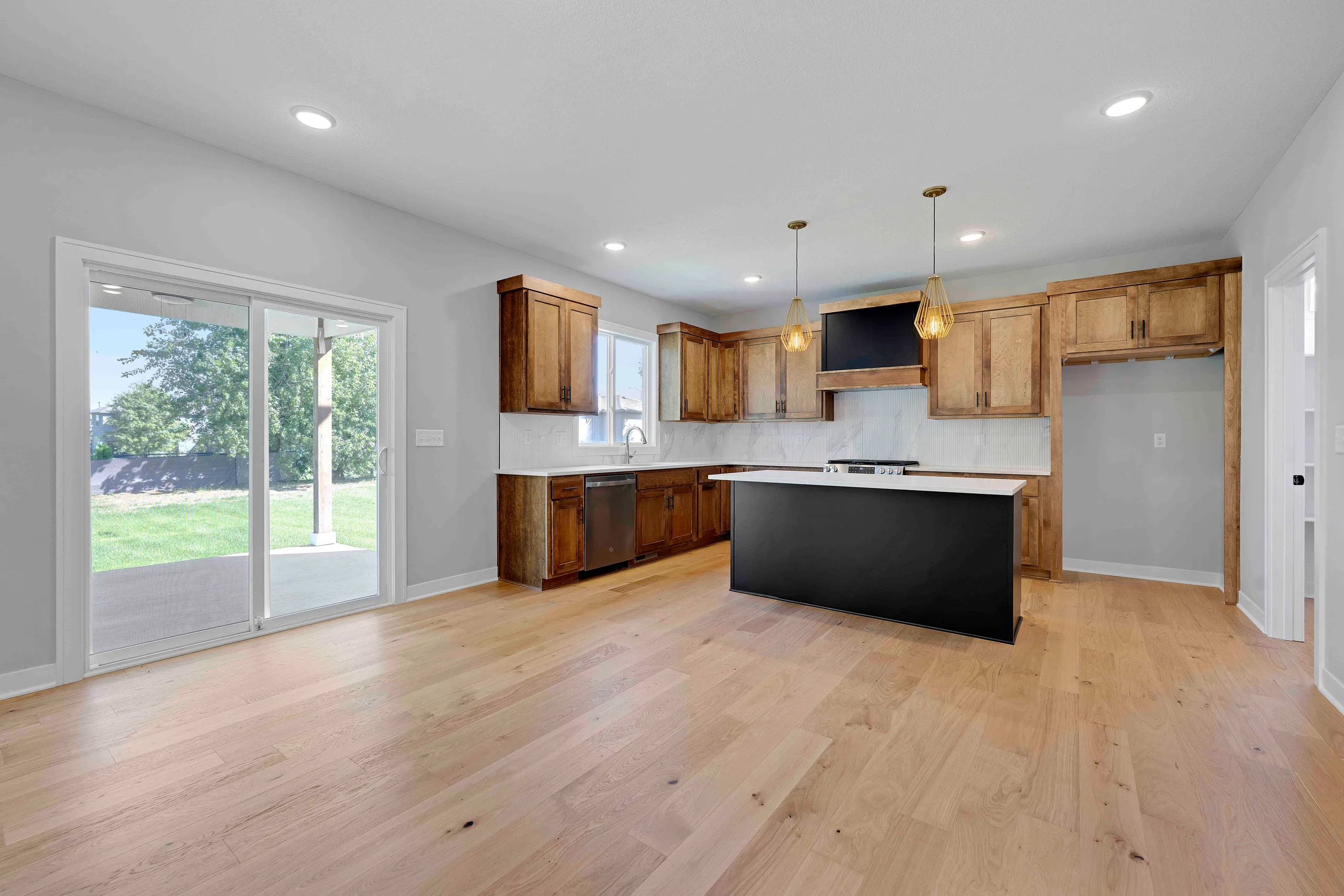 Kitchen with wood cabinetry, black island with white countertop, white backsplash, and sliding glass doors opening to