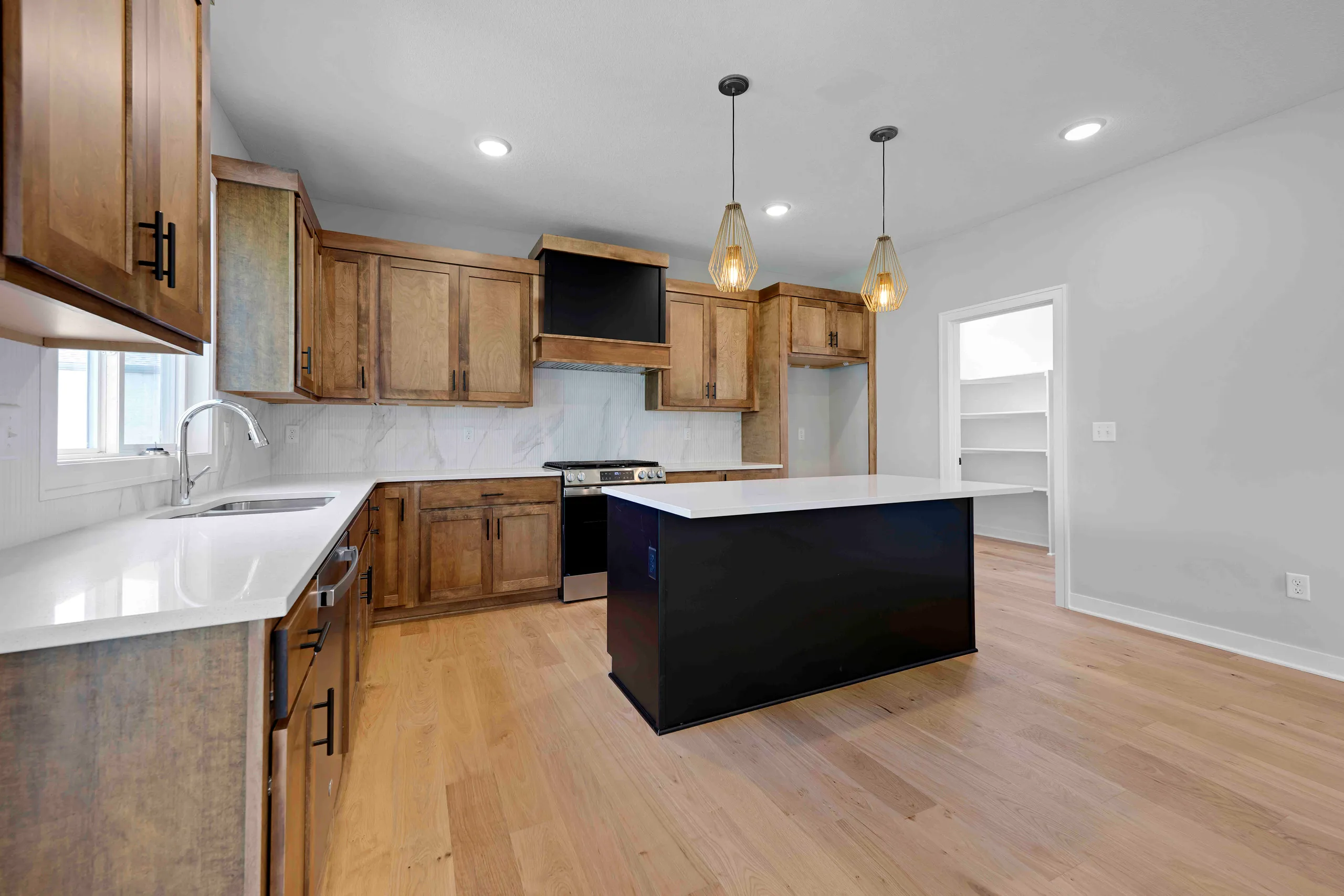 Kitchen with wood cabinets, white countertops, black island, pendant lights, and wood flooring.
