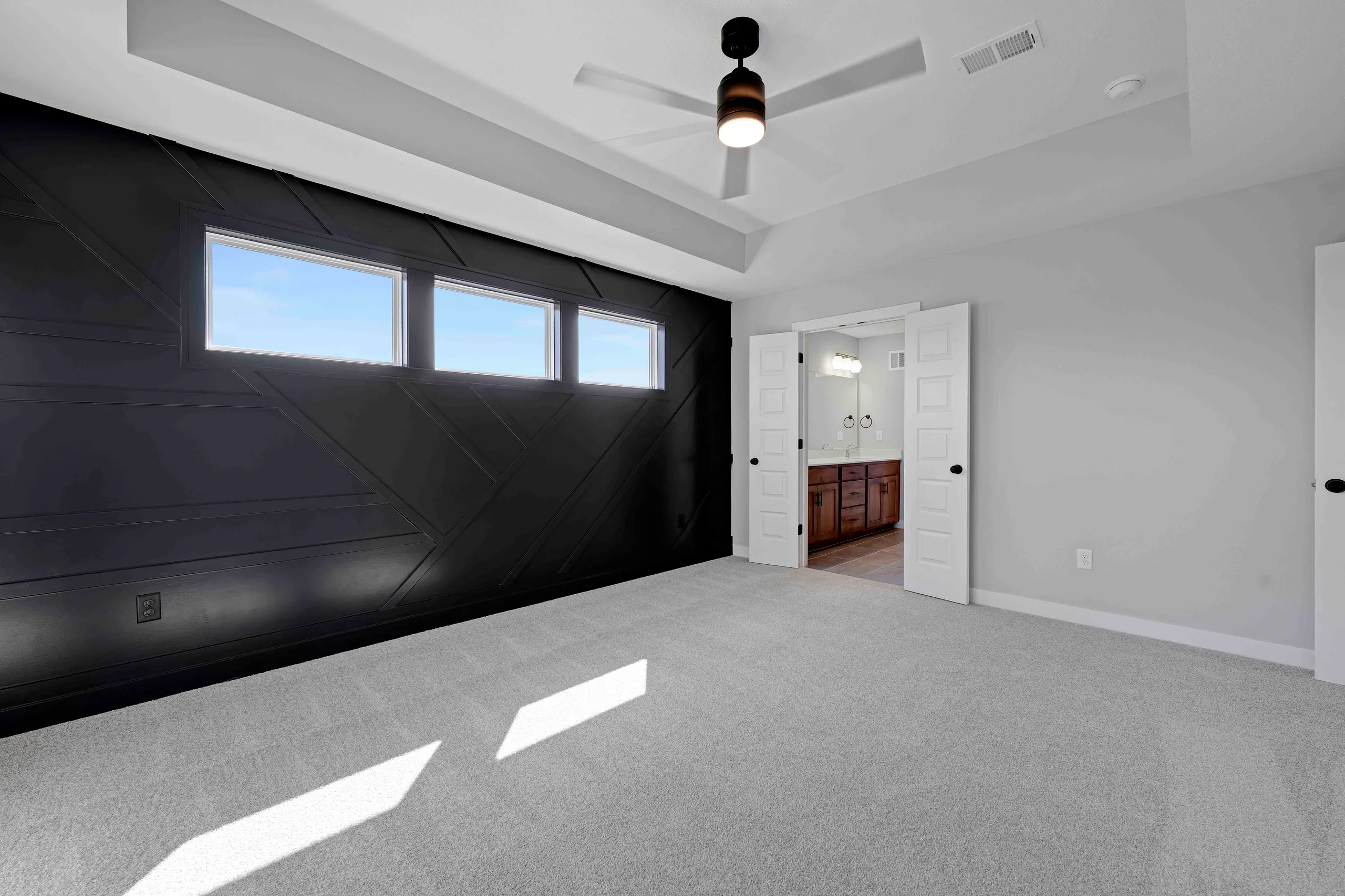 Garage interior with black paneled door and three windows, ceiling fan, and doorway leading to bathroom with wood vanity.