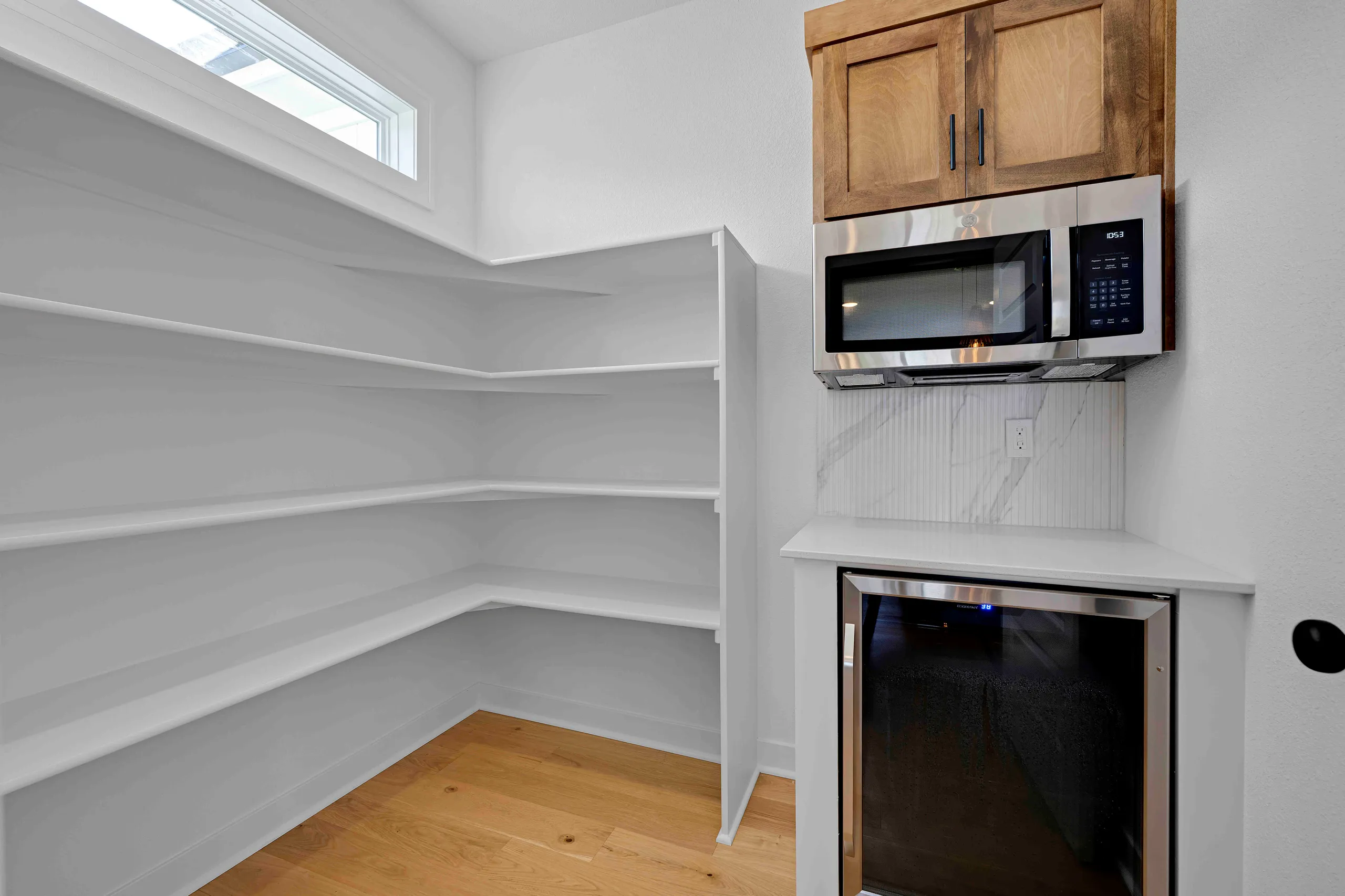 Kitchen pantry with white shelving, wood flooring, and stainless steel microwave and oven on the right wall.